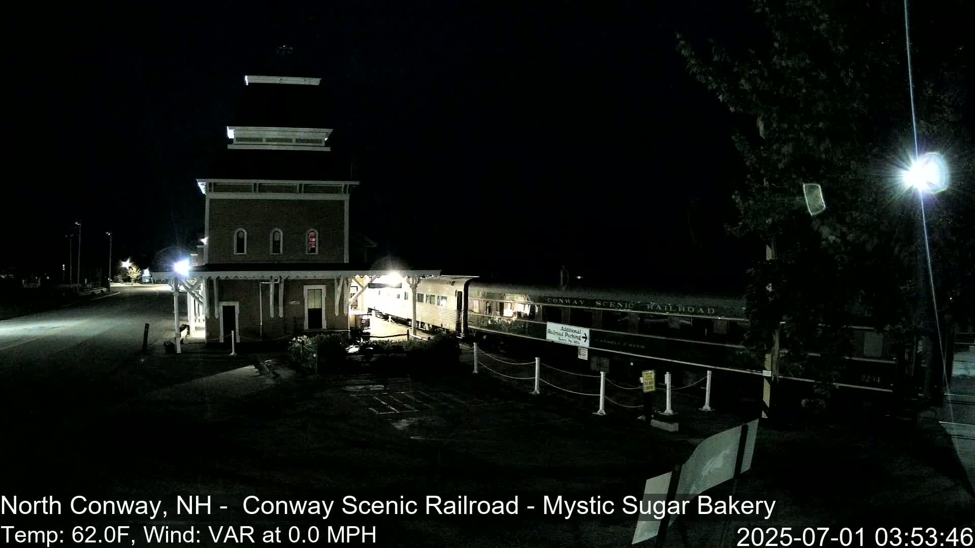 A train is parked at night next to a tall, light-colored building, under a clear, dark sky.