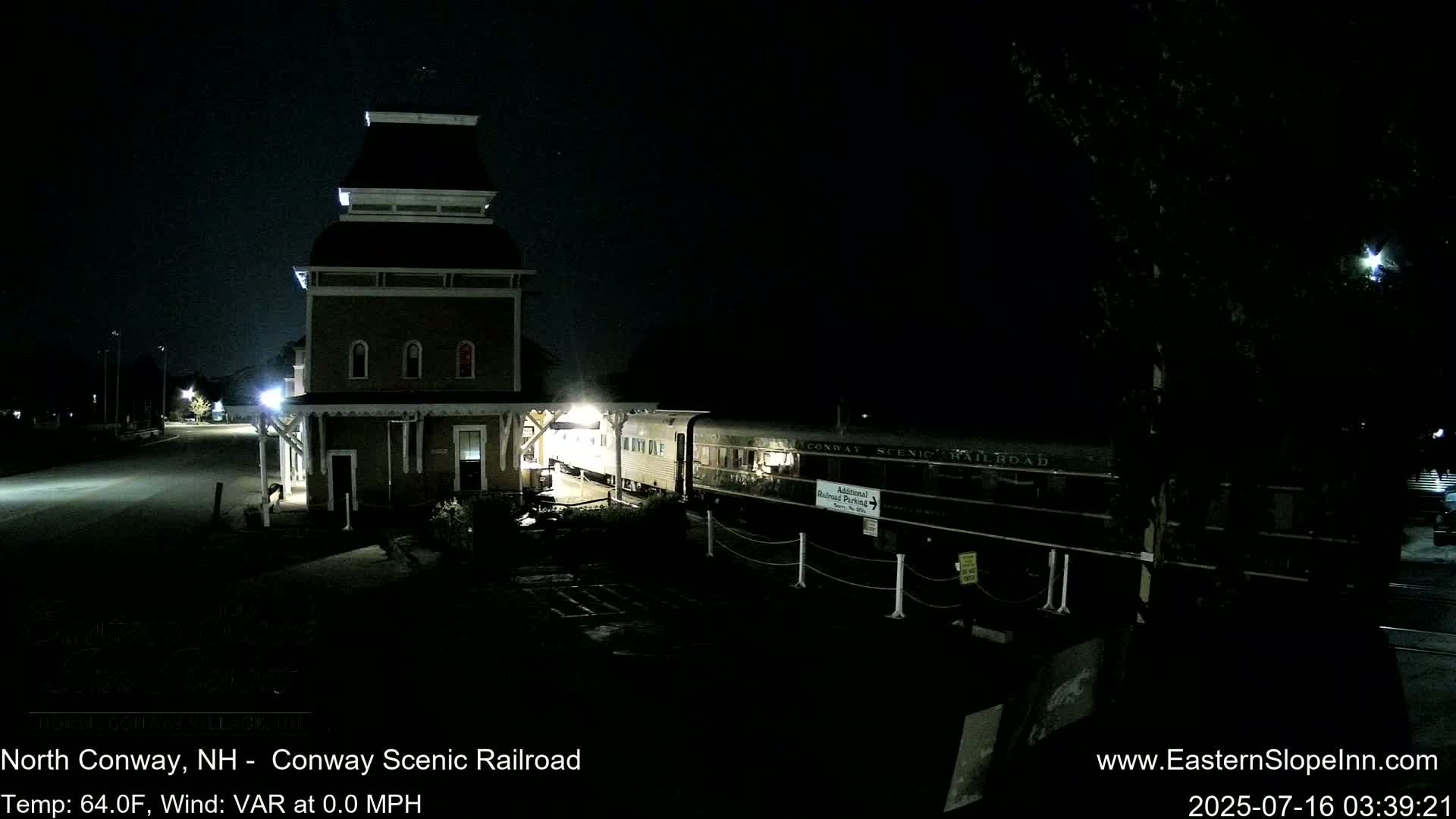 A train is parked at night next to a tall, brown building.