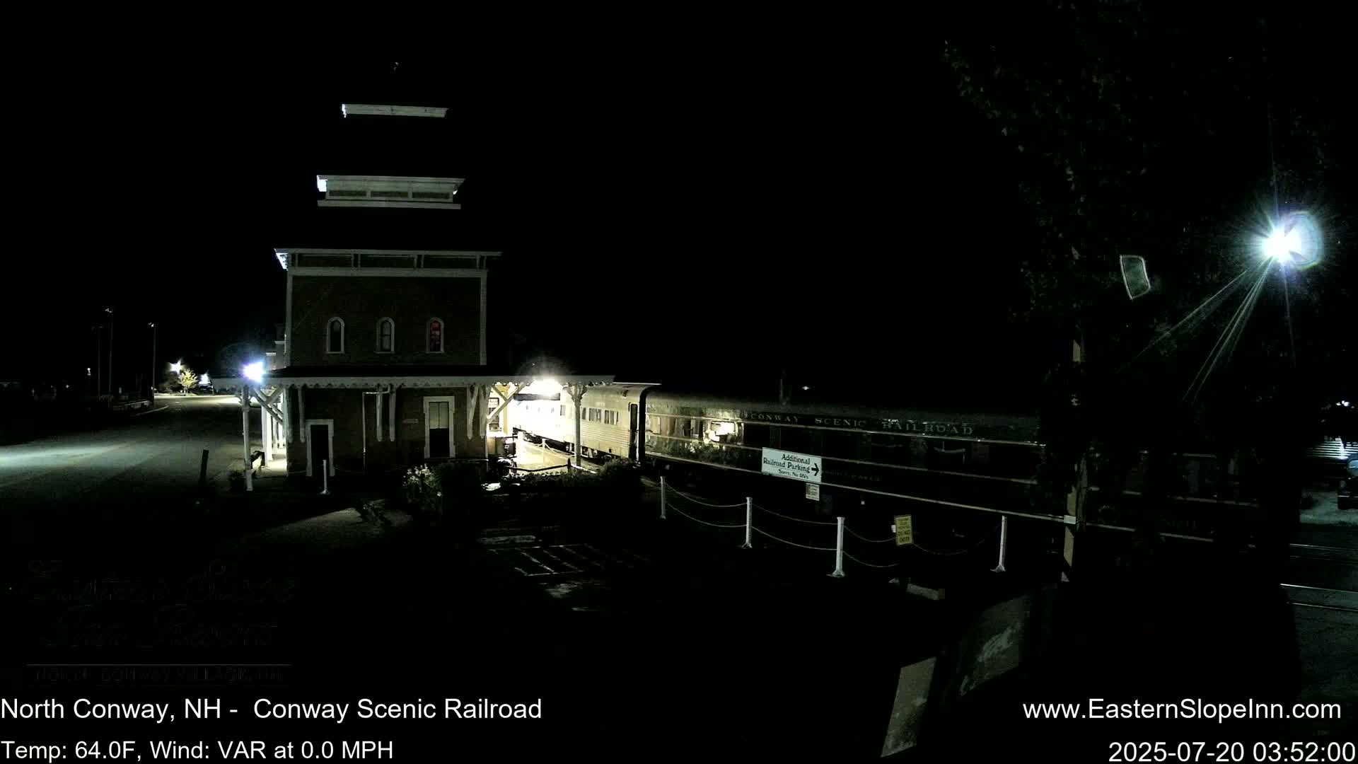 A passenger train is stopped at a nighttime station next to a tall building under a dark sky.