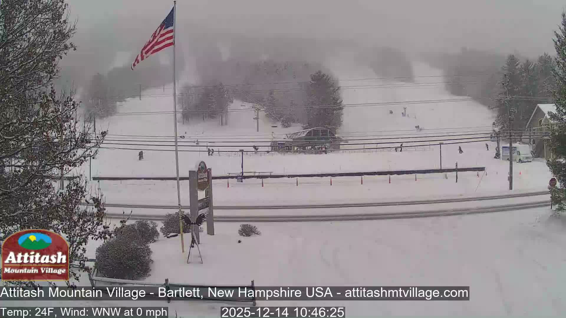 A dark outdoor scene at night reveals a hazy or misty atmosphere illuminated by artificial lights over a road, with an American flag visible on a pole and indistinct trees in the background.