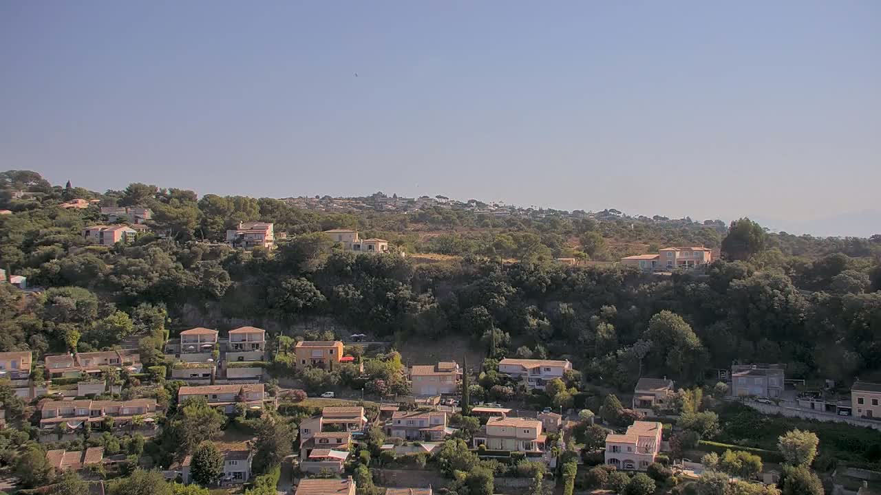A hillside covered in lush green vegetation and dotted with numerous houses, under a clear, bright sky.