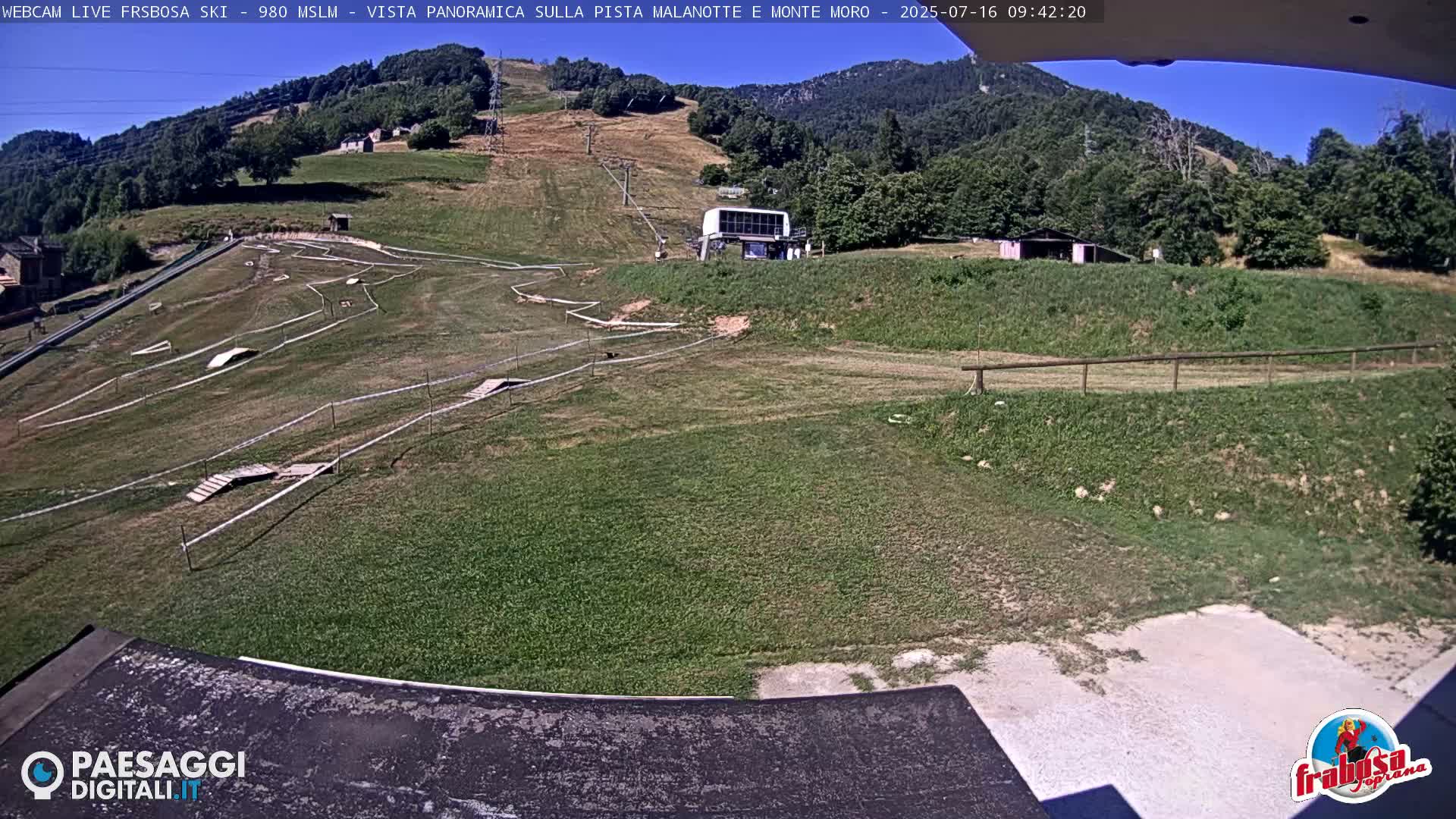 A grassy hillside with a mountain biking course and a ski lift station visible under a clear blue sky.