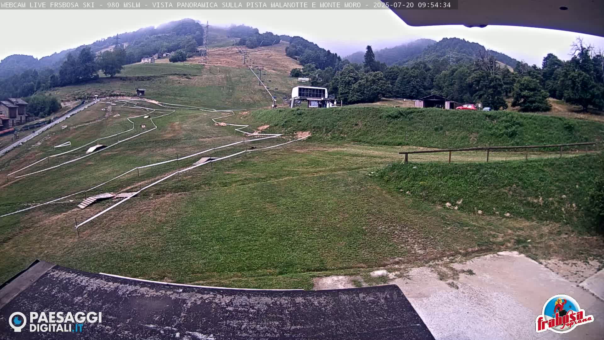 A grassy hillside with a mountain bike course and a ski lift is visible under an overcast sky.