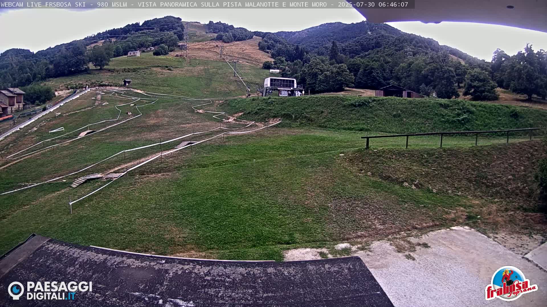 A grassy hillside with a mountain bike course and a ski lift is visible under an overcast sky.
