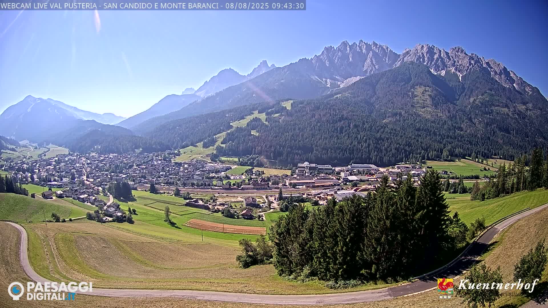 A sunny valley town nestled below a large, imposing mountain range.