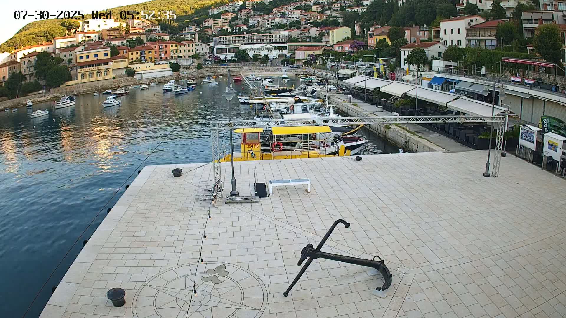 A harbor with numerous boats, a yellow submarine, and several people on a paved area, under a partly cloudy sky.