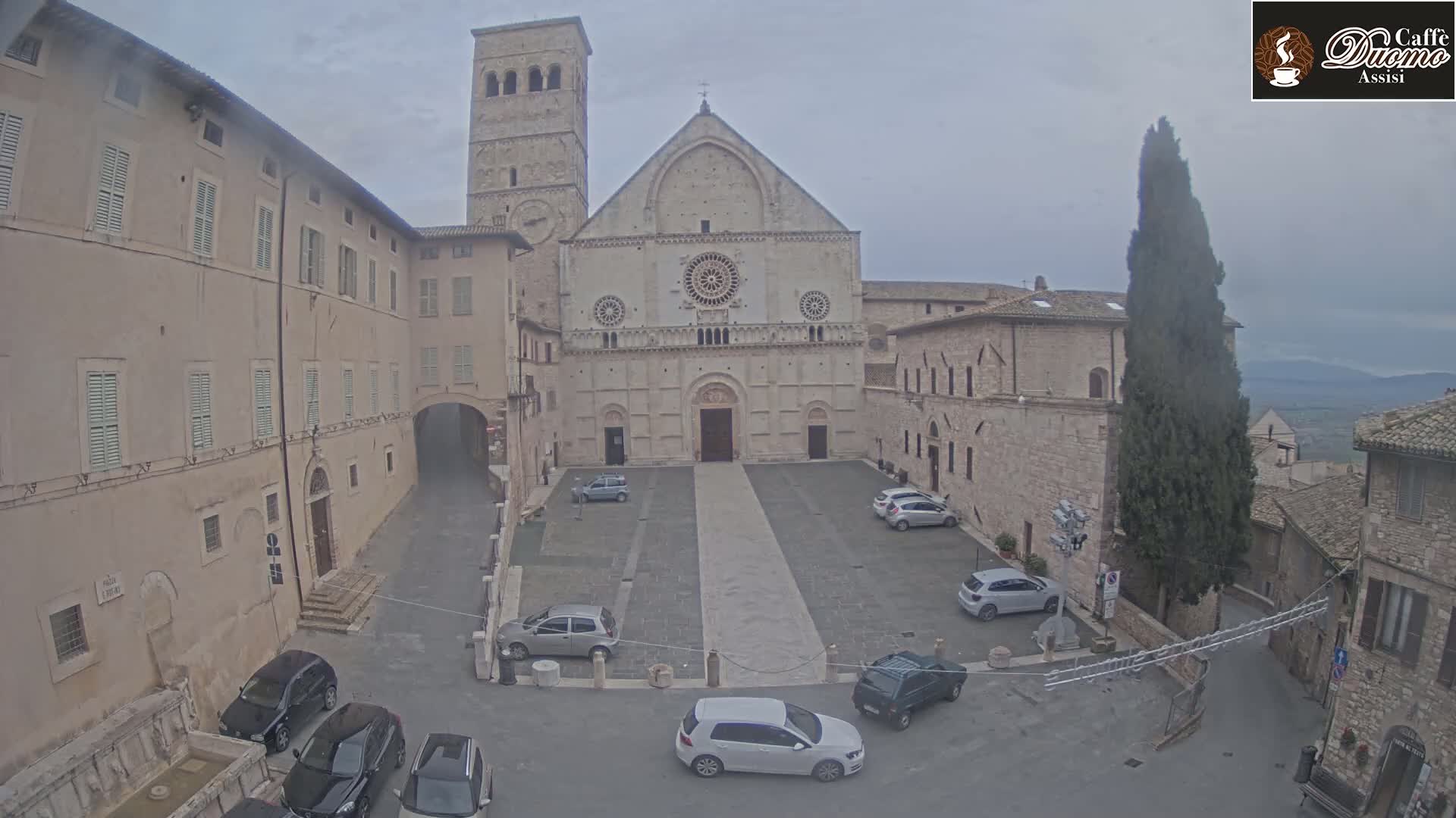 A large stone church with a square in front, surrounded by other buildings, on an overcast day.