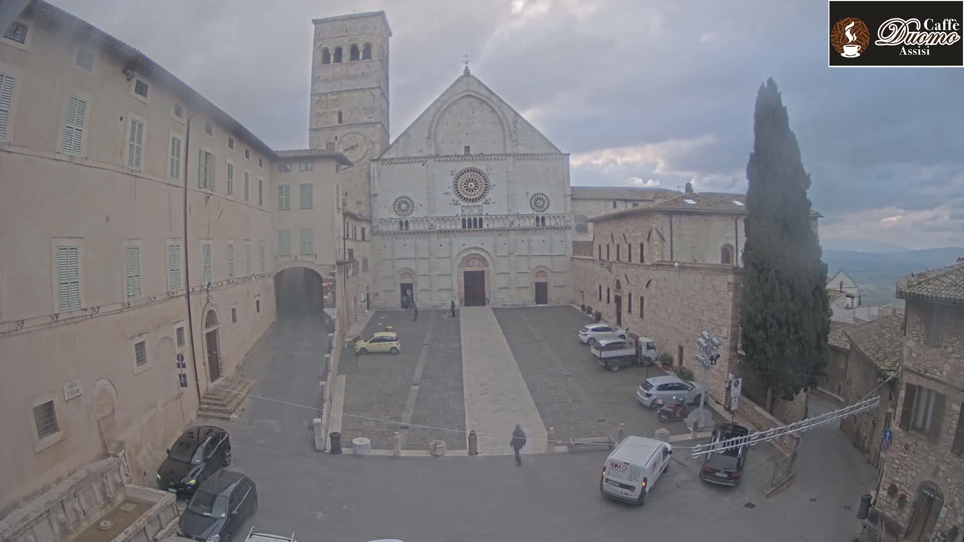 A large stone church stands in a plaza, surrounded by buildings, under an overcast sky.