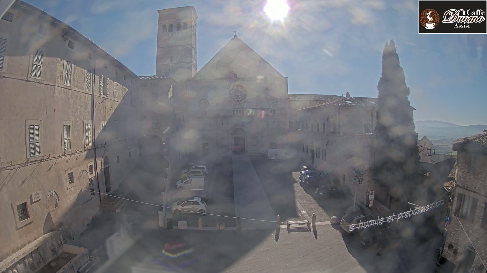 A sunny day reveals a courtyard with parked cars, surrounded by ancient stone buildings, including a large church with a rose window.