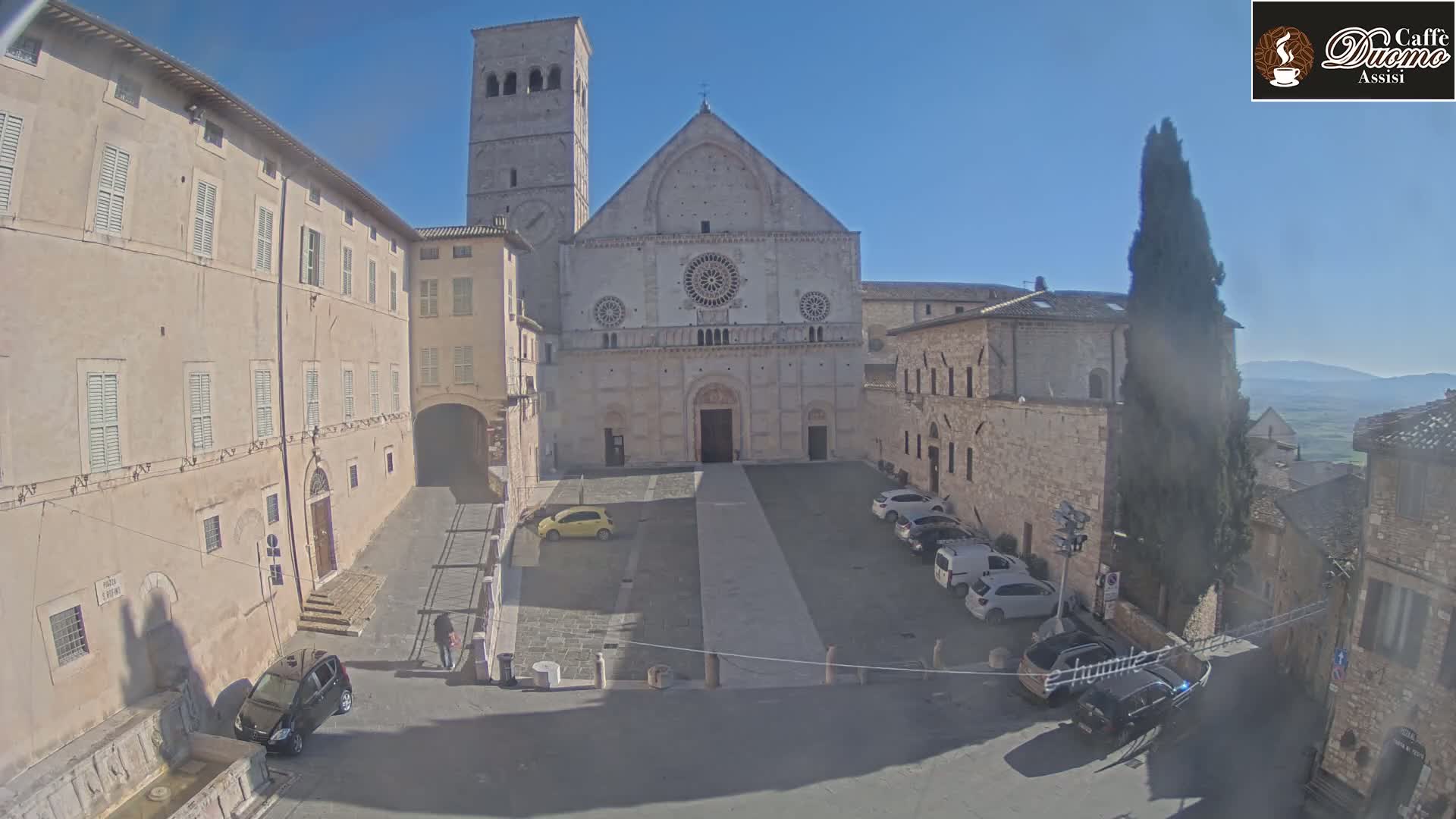 A large stone cathedral sits in a plaza surrounded by other stone buildings under a clear, sunny sky.