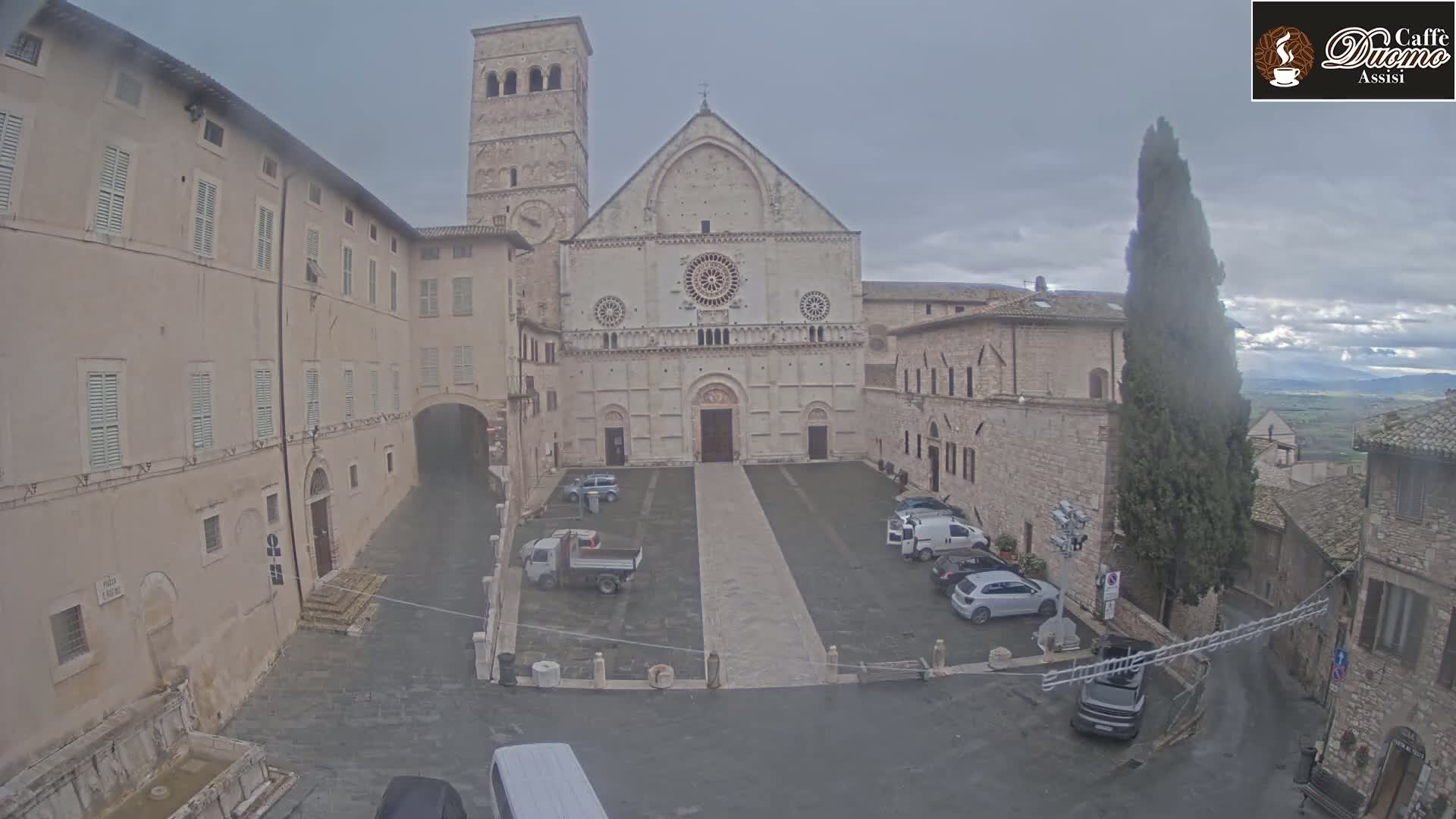 A stone plaza with a large cathedral and surrounding buildings is seen on an overcast day.
