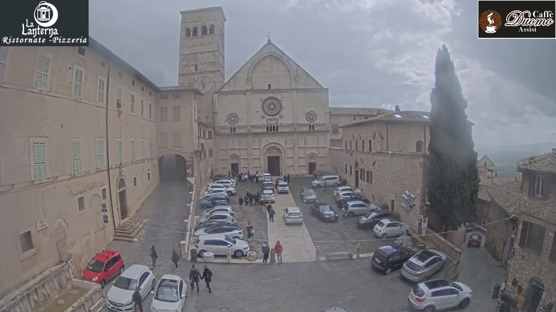 A stone plaza with parked cars in front of a large stone church under an overcast sky.