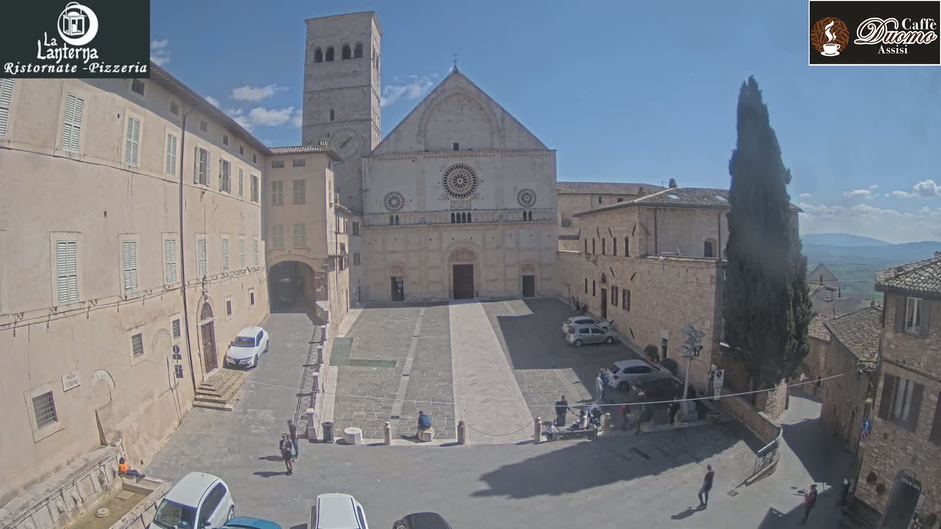 A sunny day reveals a town square in Italy, centered on a large stone cathedral, surrounded by buildings and a few people.