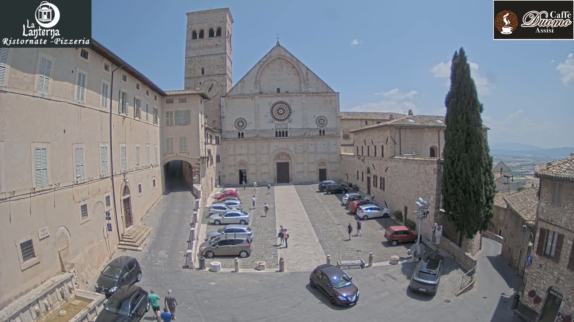 A sunny day reveals a town square with parked cars, pedestrians, and a large stone church as a backdrop.