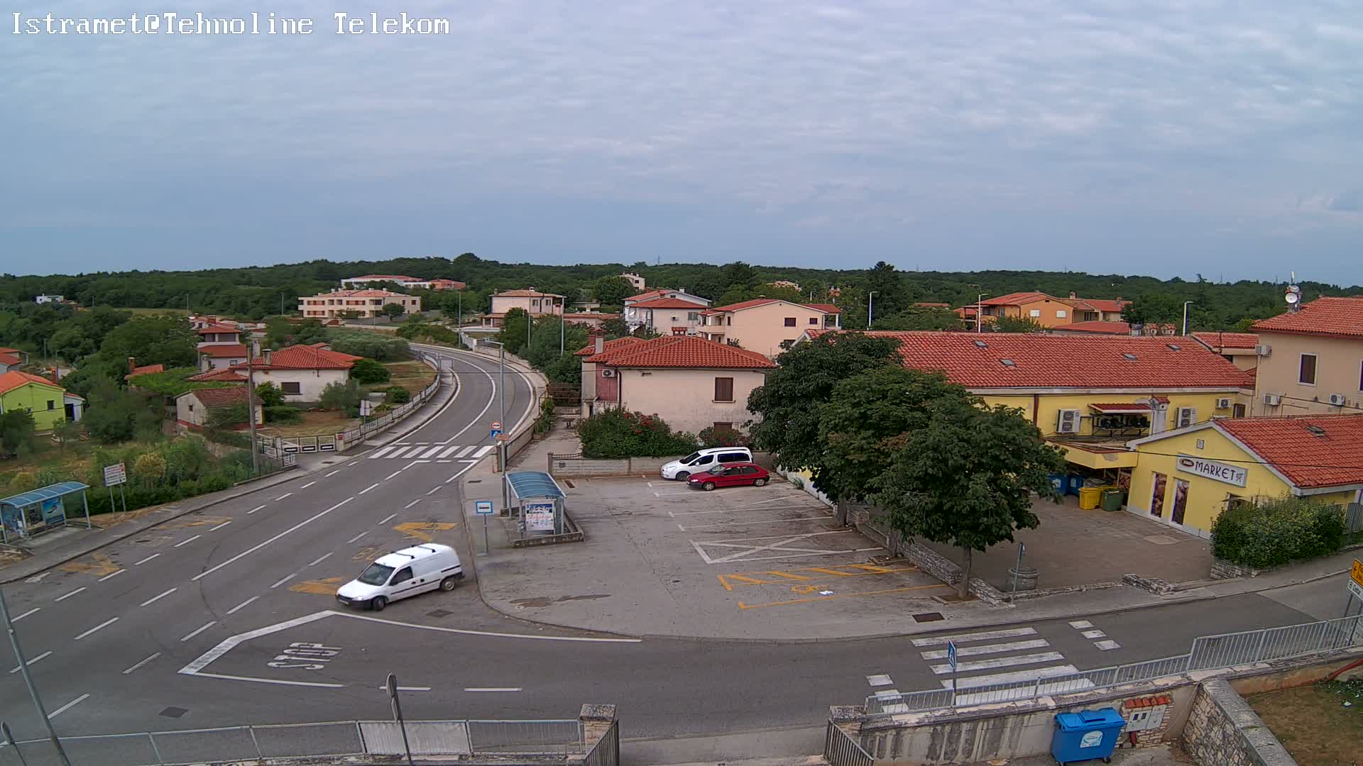 A high-angle view of a small town on an overcast day, showing a road intersection with a few cars and a small market.