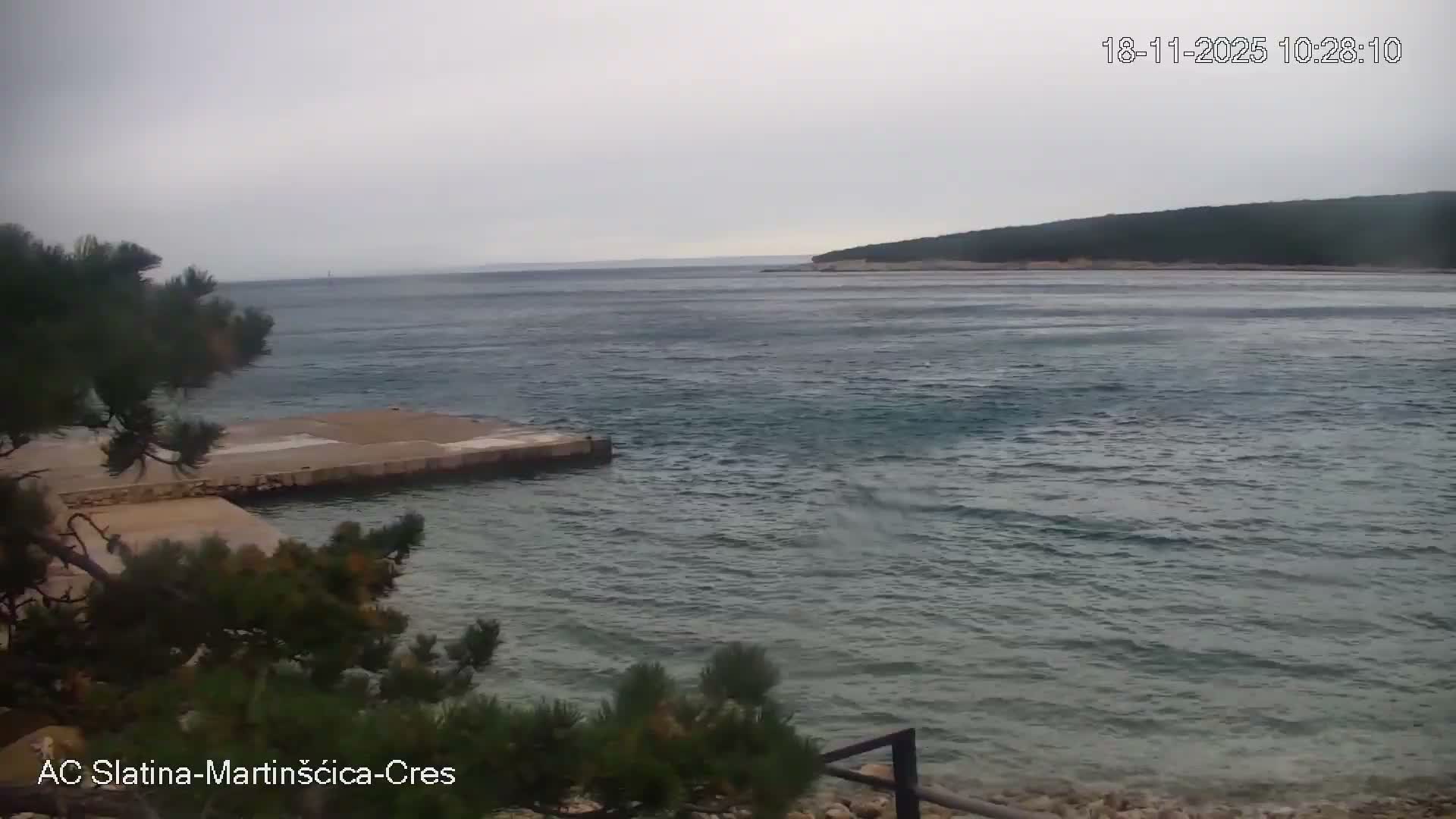 A pebble beach with clear, blue water and an inflatable water park is visible on a sunny day.