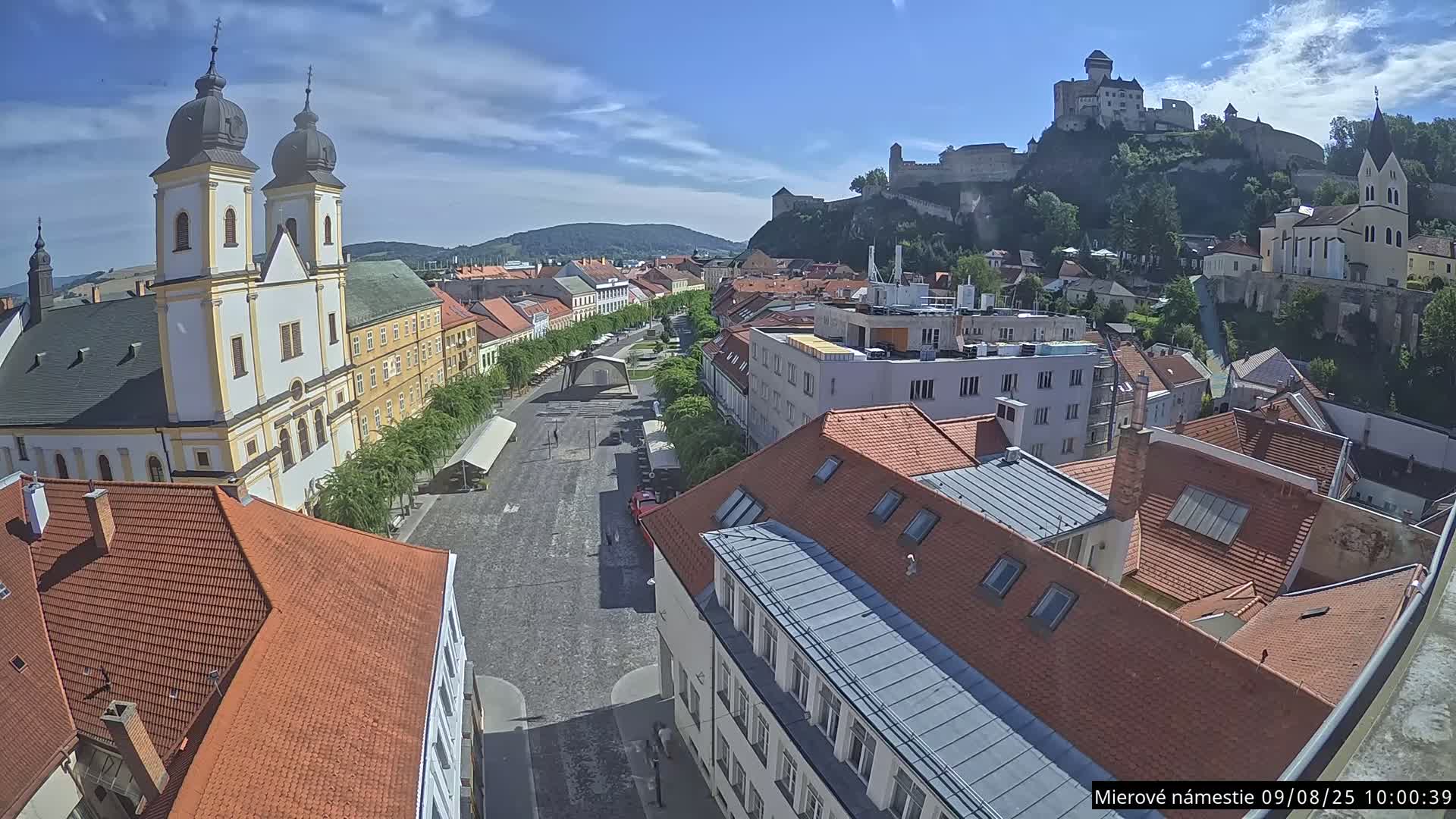 A high-angle, sunny view of a town square with a church and castle visible in the distance.