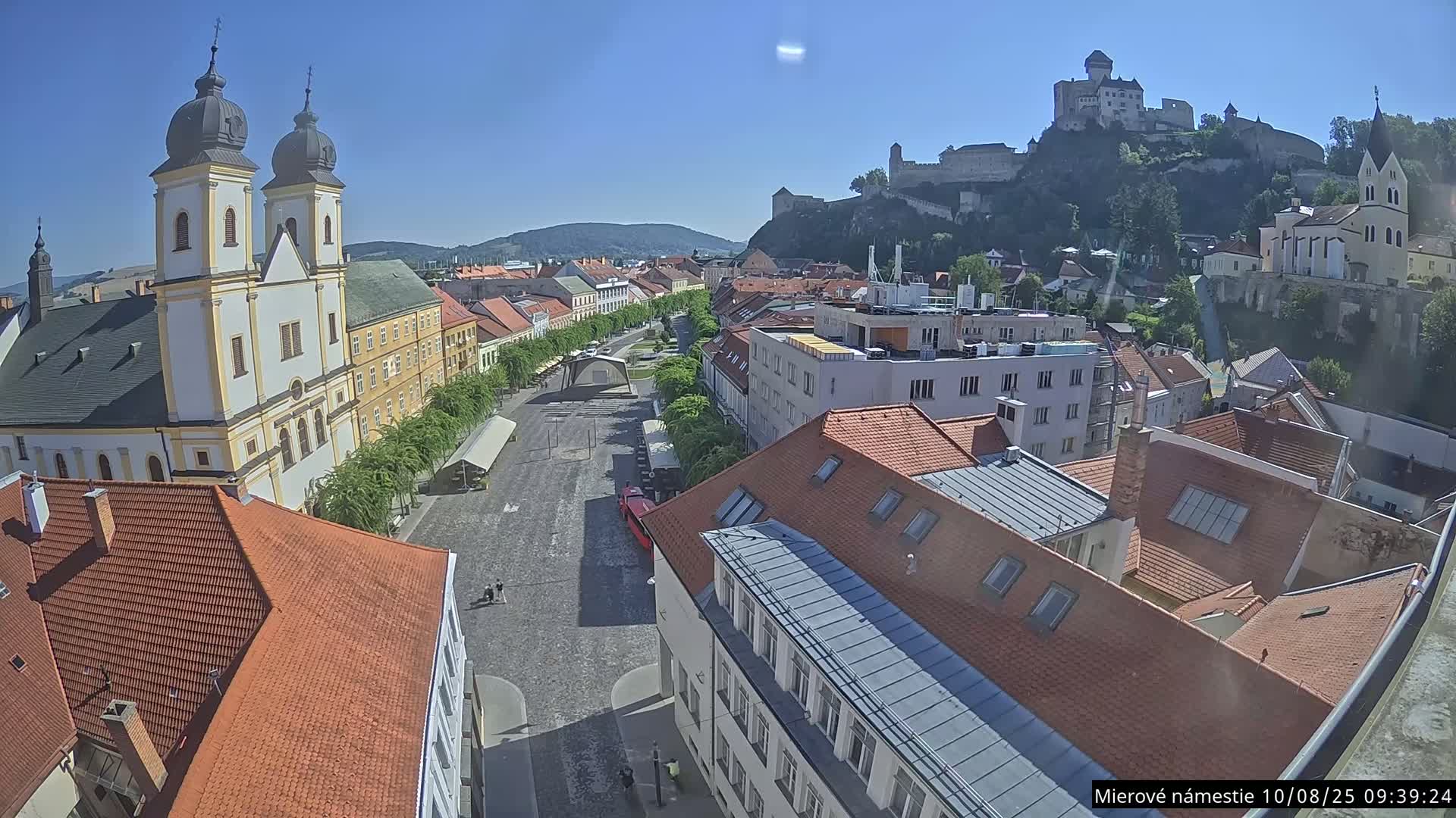 A high-angle view shows a town square on a sunny day, with a church and a castle visible in the background.