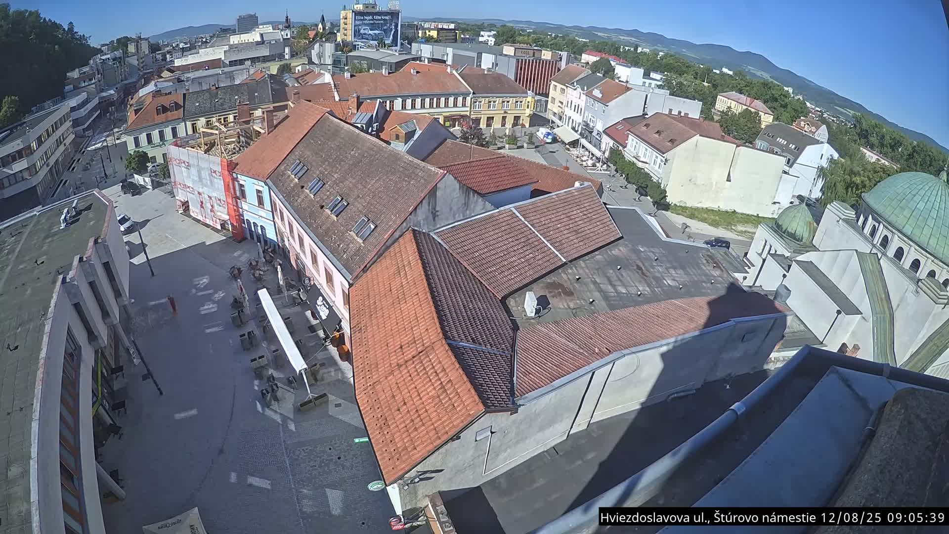 A high-angle view shows a town square with many buildings under a clear, sunny sky.