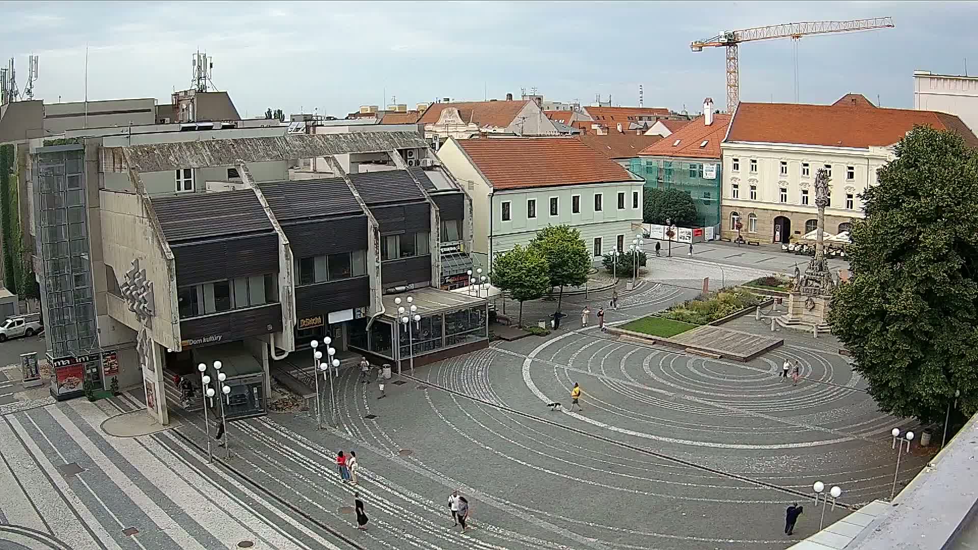 An overcast day reveals a town square with a circular, patterned plaza, surrounded by buildings and a few pedestrians.