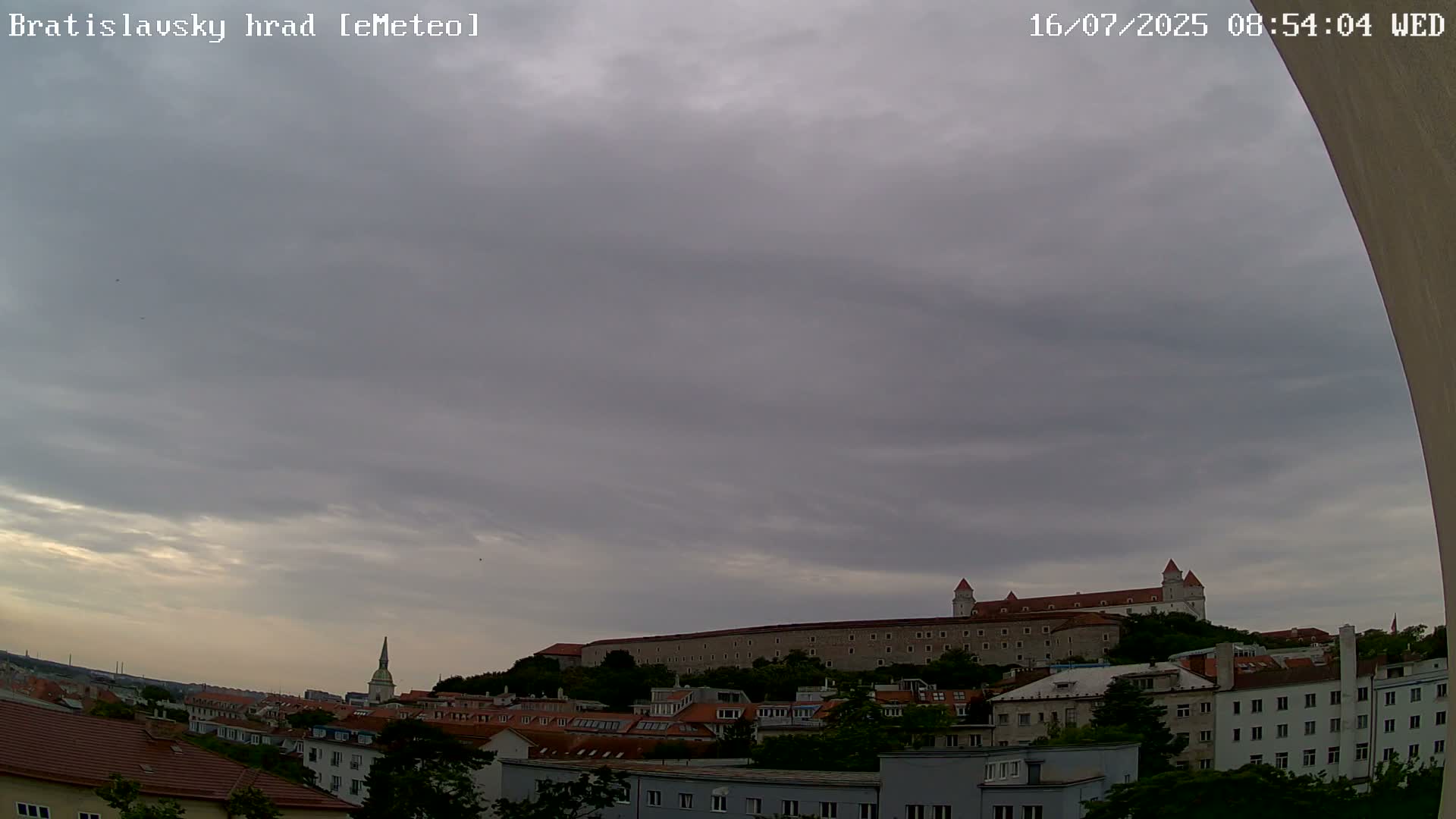 A large stone castle sits atop a hill overlooking a city under an overcast sky.