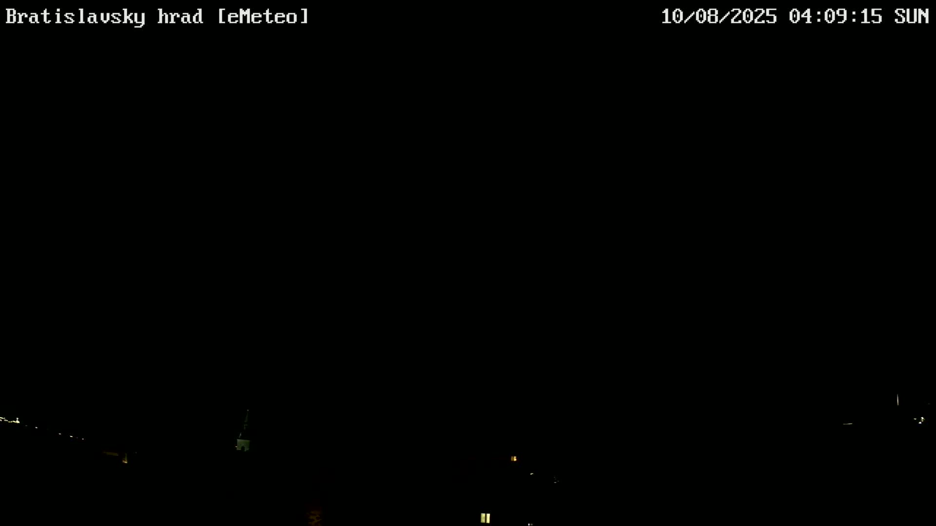 A nighttime, dark image shows dimly lit buildings and structures at the bottom of the frame under a clear, black sky.