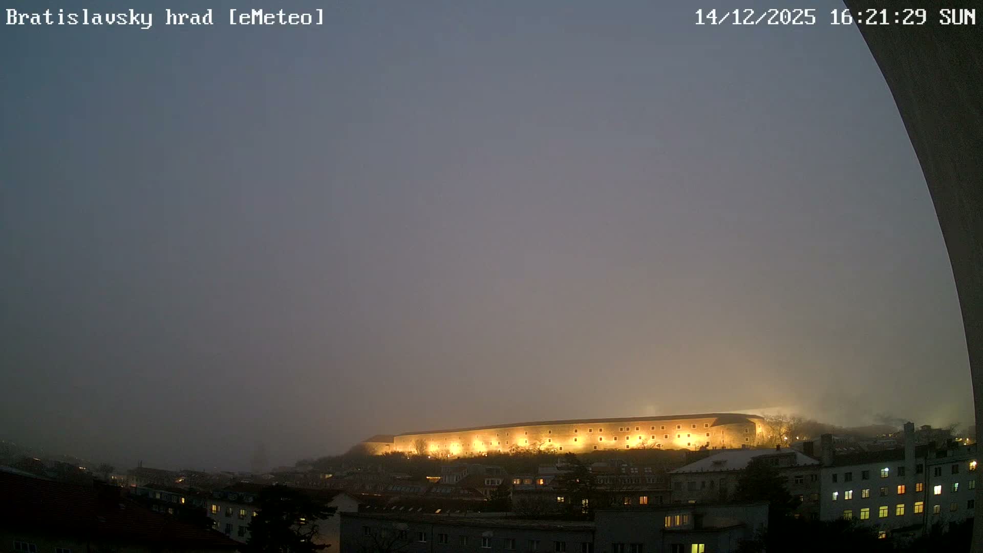 A city and a prominent castle-like building are dimly visible in the distance, largely obscured by dense fog or mist under heavily overcast skies.