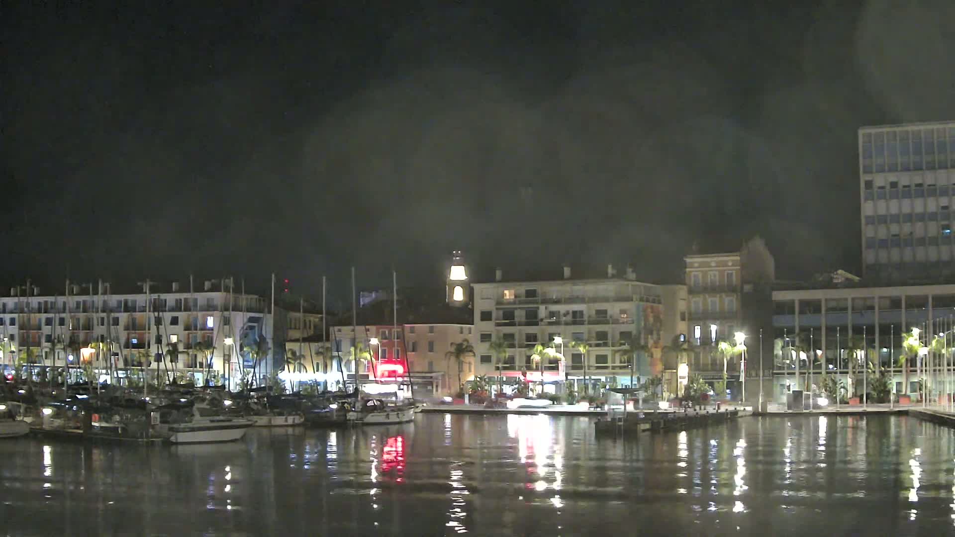 A large cruise ship and a smaller yacht are docked in calm water under a cloudy sky.