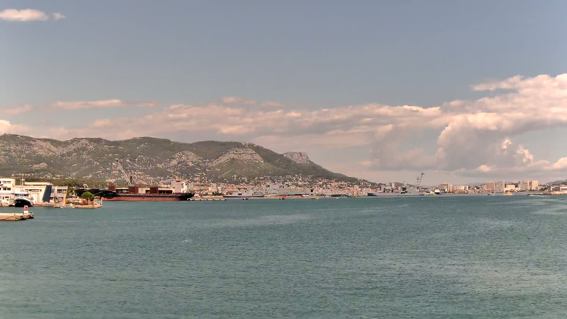 A large cruise ship and a smaller yacht are docked in calm water under a cloudy sky.