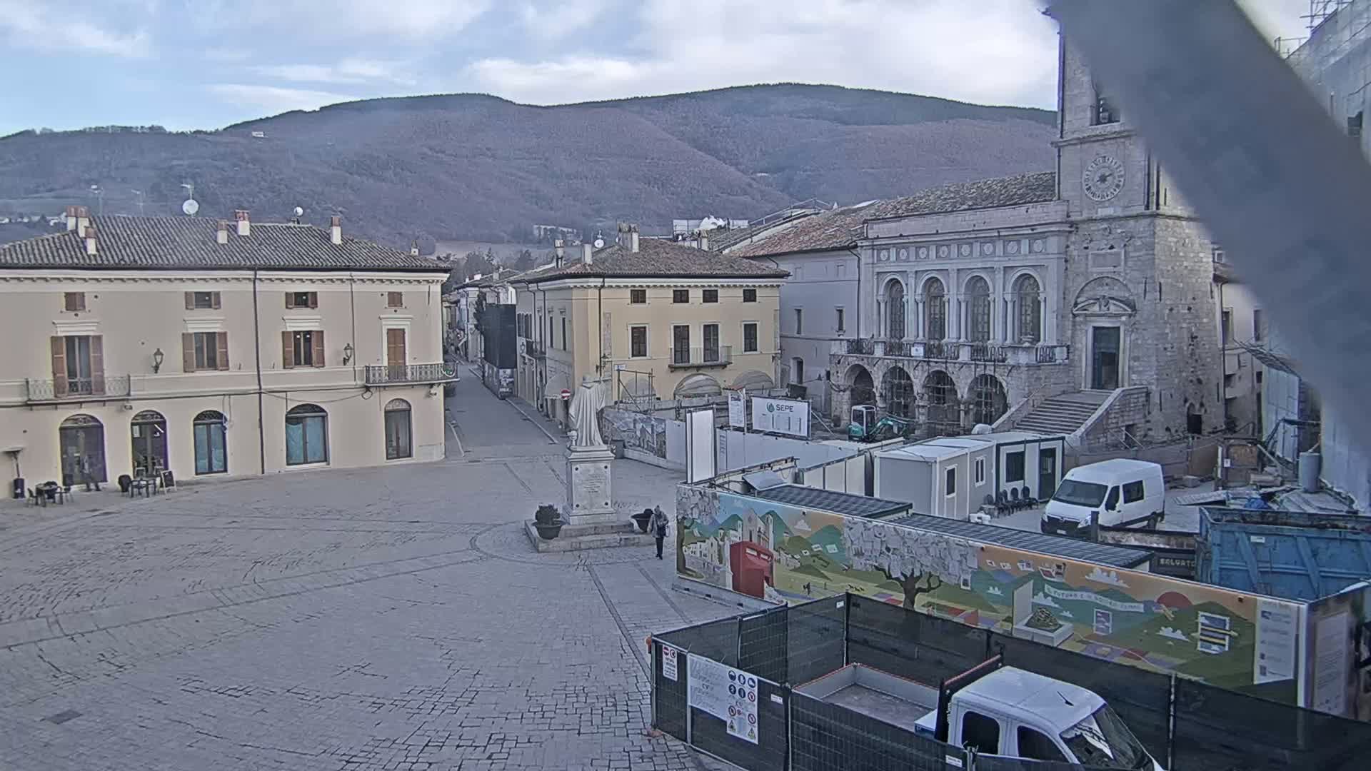 A town square with several buildings, a statue, construction equipment, and overcast skies.