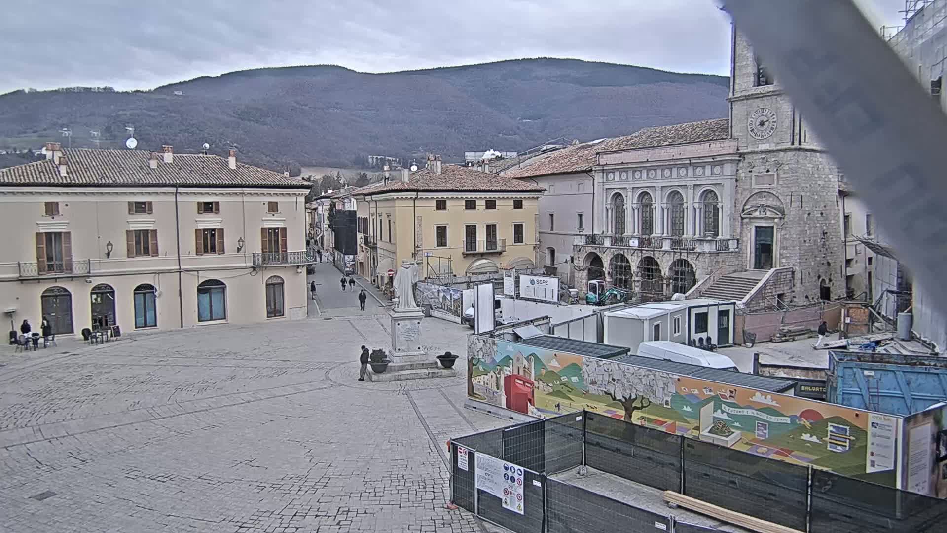 A town square under an overcast sky, with buildings surrounding it and construction work underway in the center.
