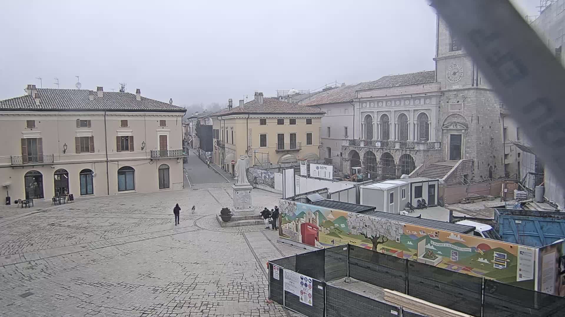 A town square with several buildings, a statue, and construction materials is visible under an overcast sky.