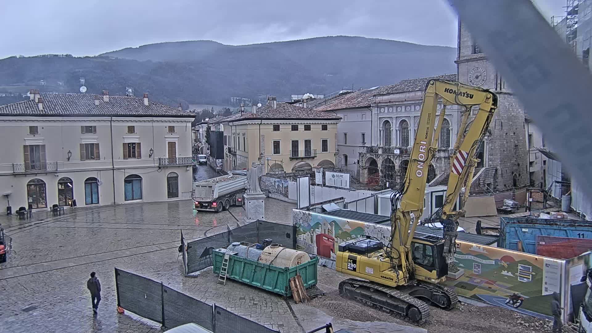 A town square under an overcast sky, with construction equipment and dump trucks in the midst of a renovation project.