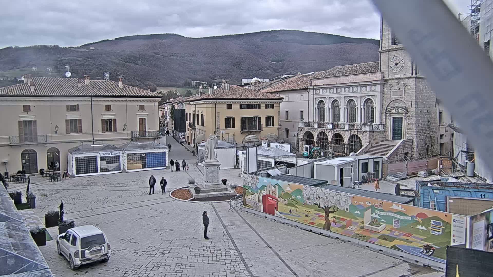 A town square with several buildings, temporary structures, and a statue, under an overcast sky.