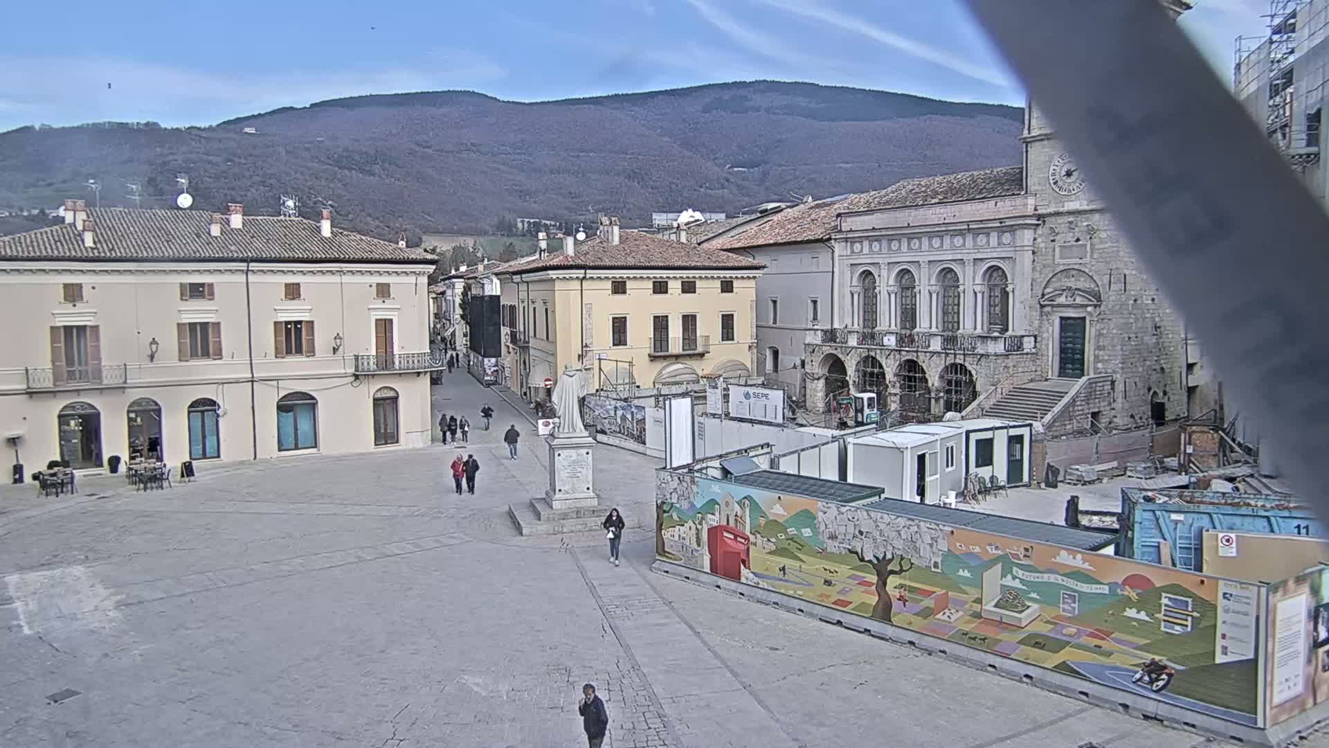 A mostly empty town square, under a clear sky, is surrounded by historic buildings, with construction underway in the center.