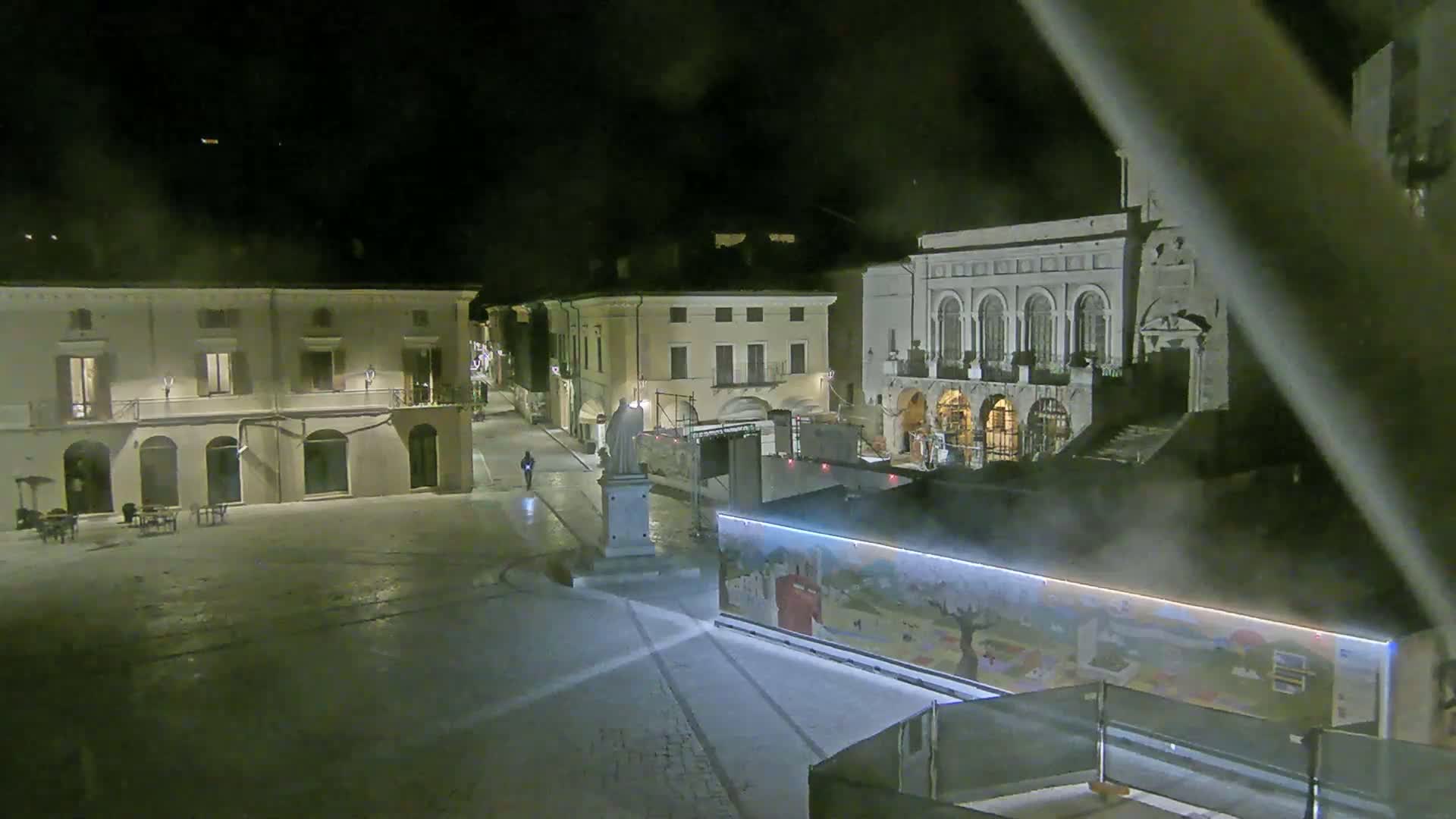 A nighttime view of a town square with several buildings, a statue, and a large painted structure, under hazy or foggy conditions.