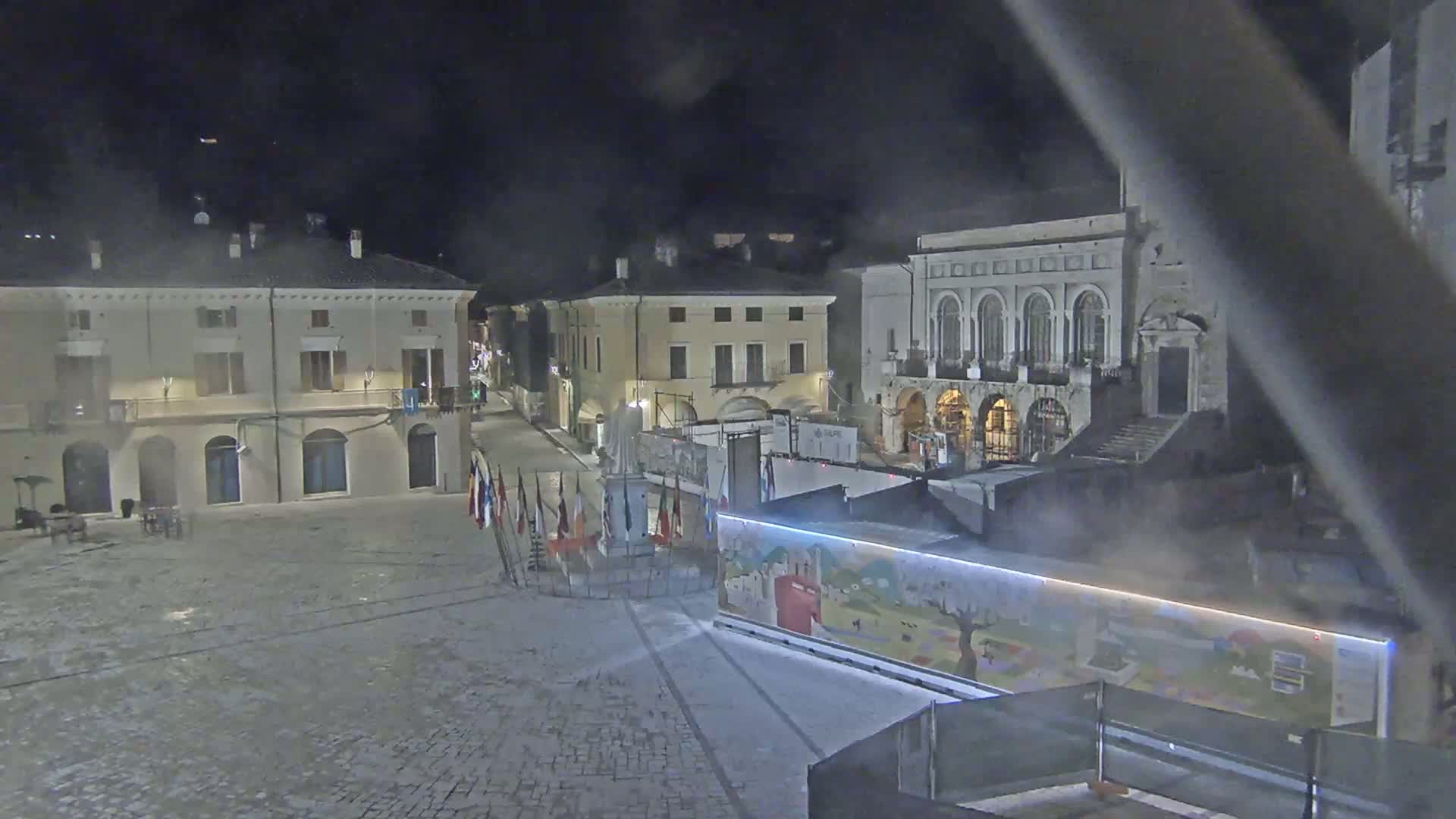 A nighttime view of a town square with several buildings, a monument, and a colorful structure, under hazy or foggy conditions.