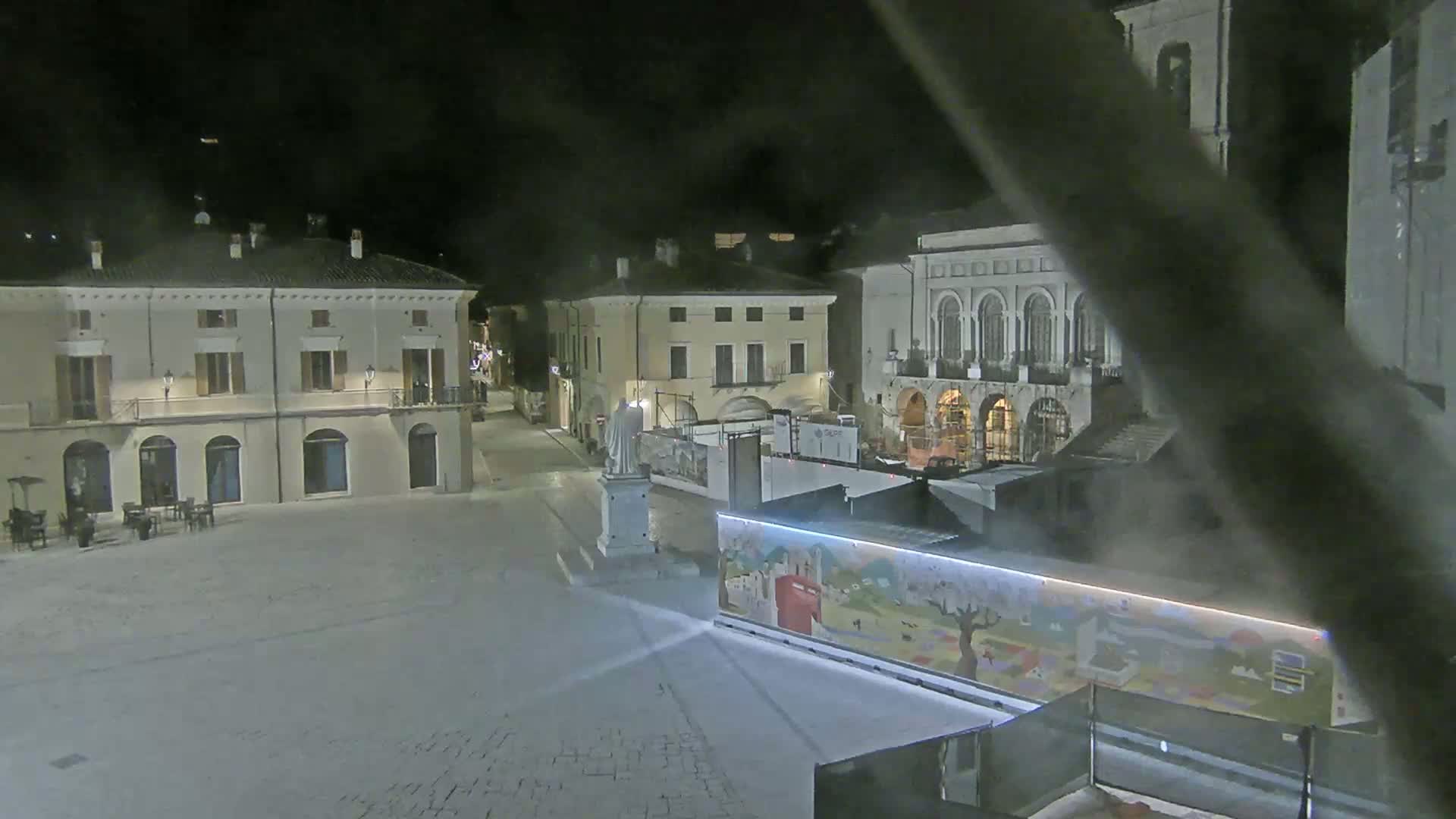 A nighttime view of a town square with several buildings, a statue, and a painted structure, under hazy or foggy conditions.