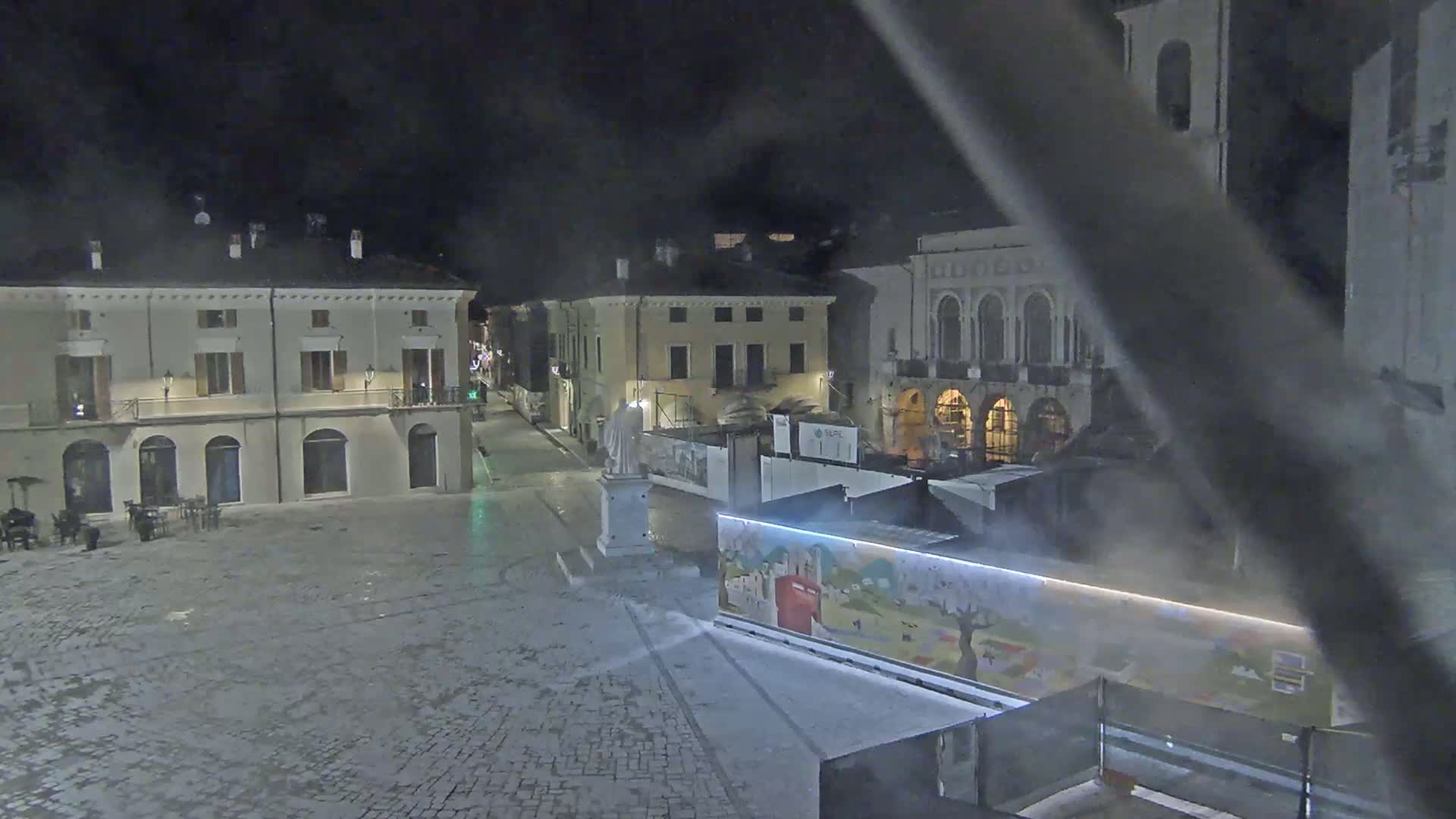 An empty town square at night, with several buildings surrounding it, is lightly misted.