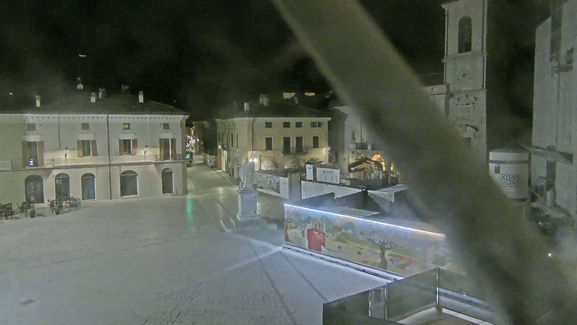A nighttime view of a cobblestone town square with several buildings, a statue, and a painted wall.