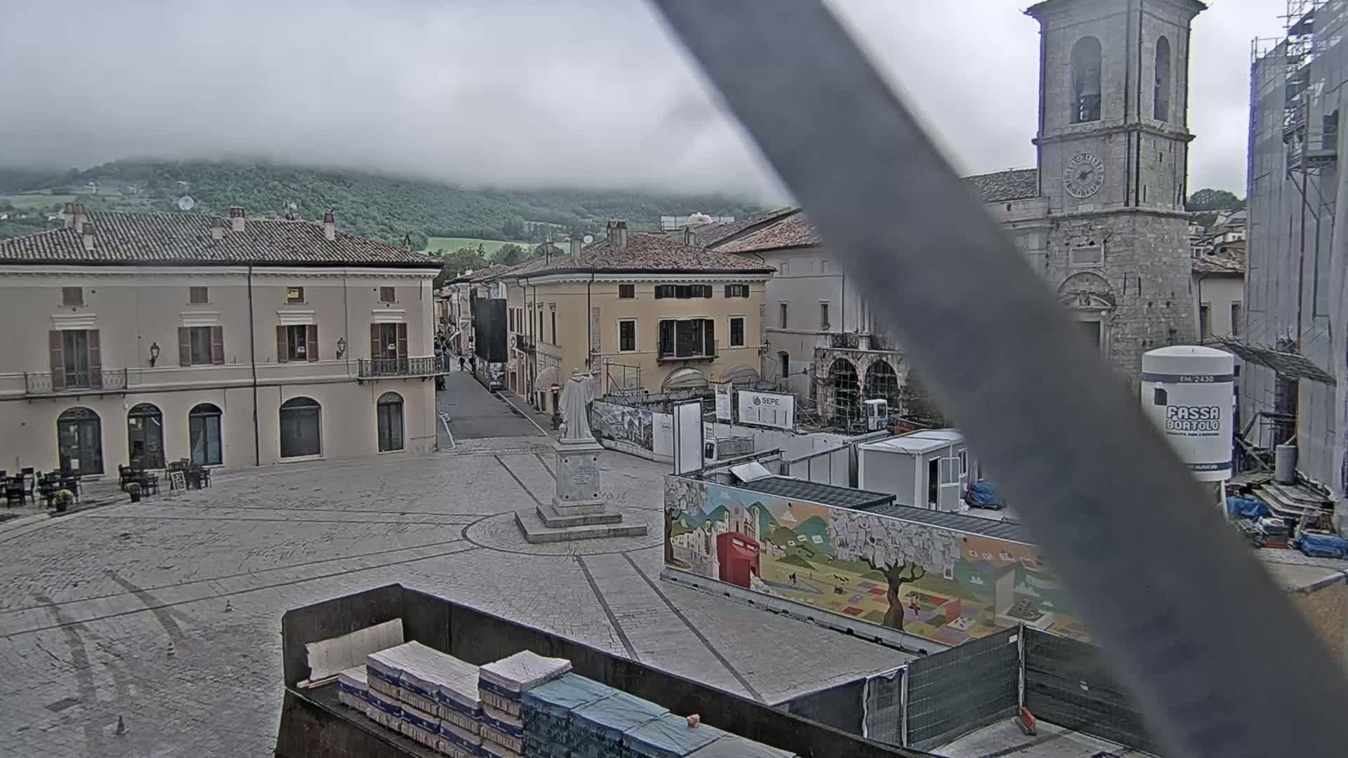 A town square, partially under construction, is viewed on an overcast day with mountains in the background.