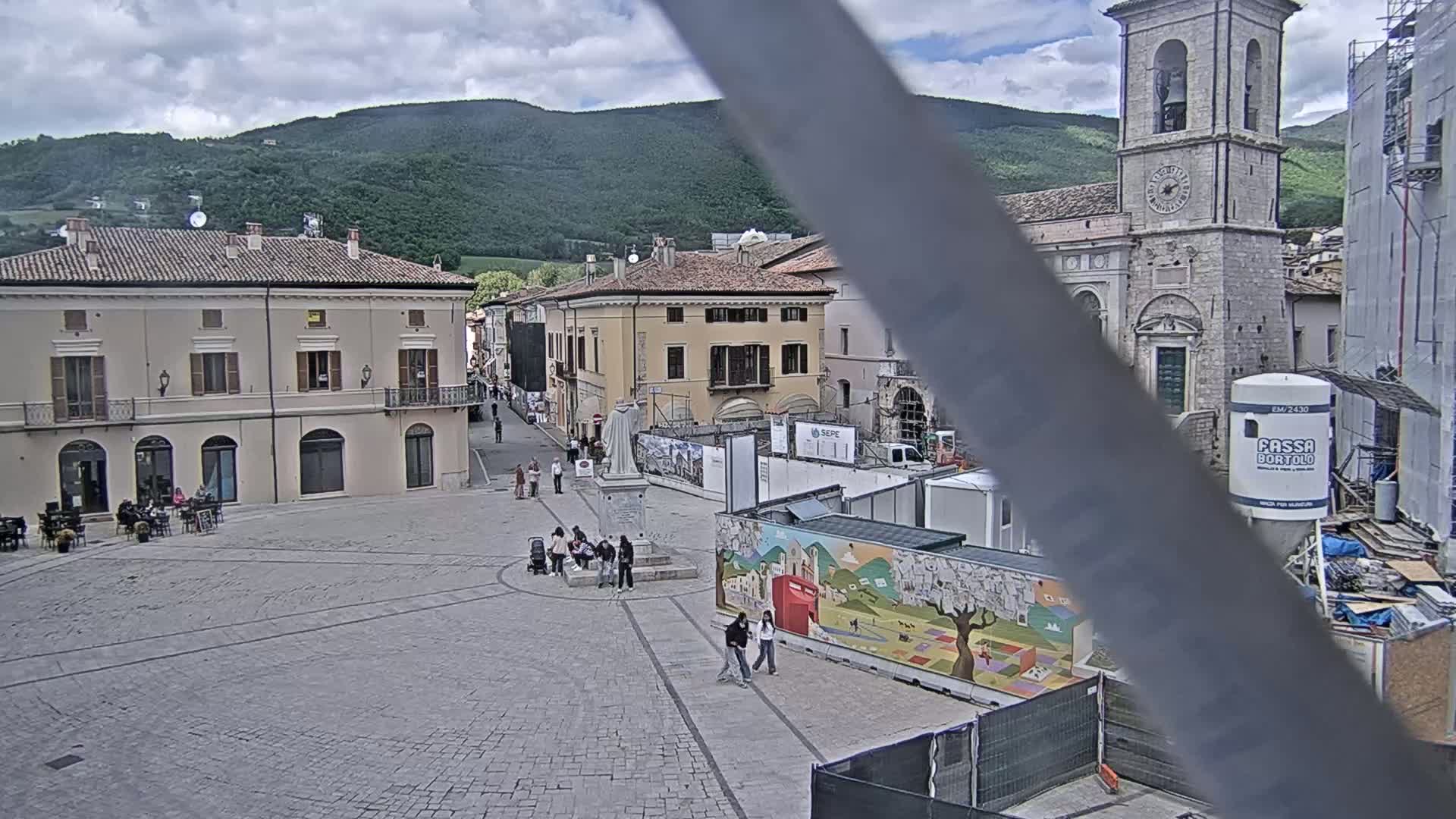 A mostly empty town square with several buildings, including a church with a bell tower, under cloudy skies.