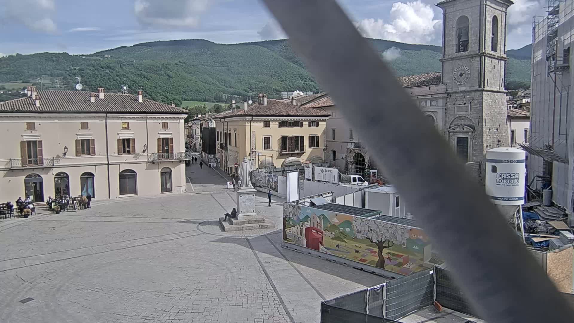 A town square with several buildings, a statue, and construction equipment is visible under a partly cloudy sky.