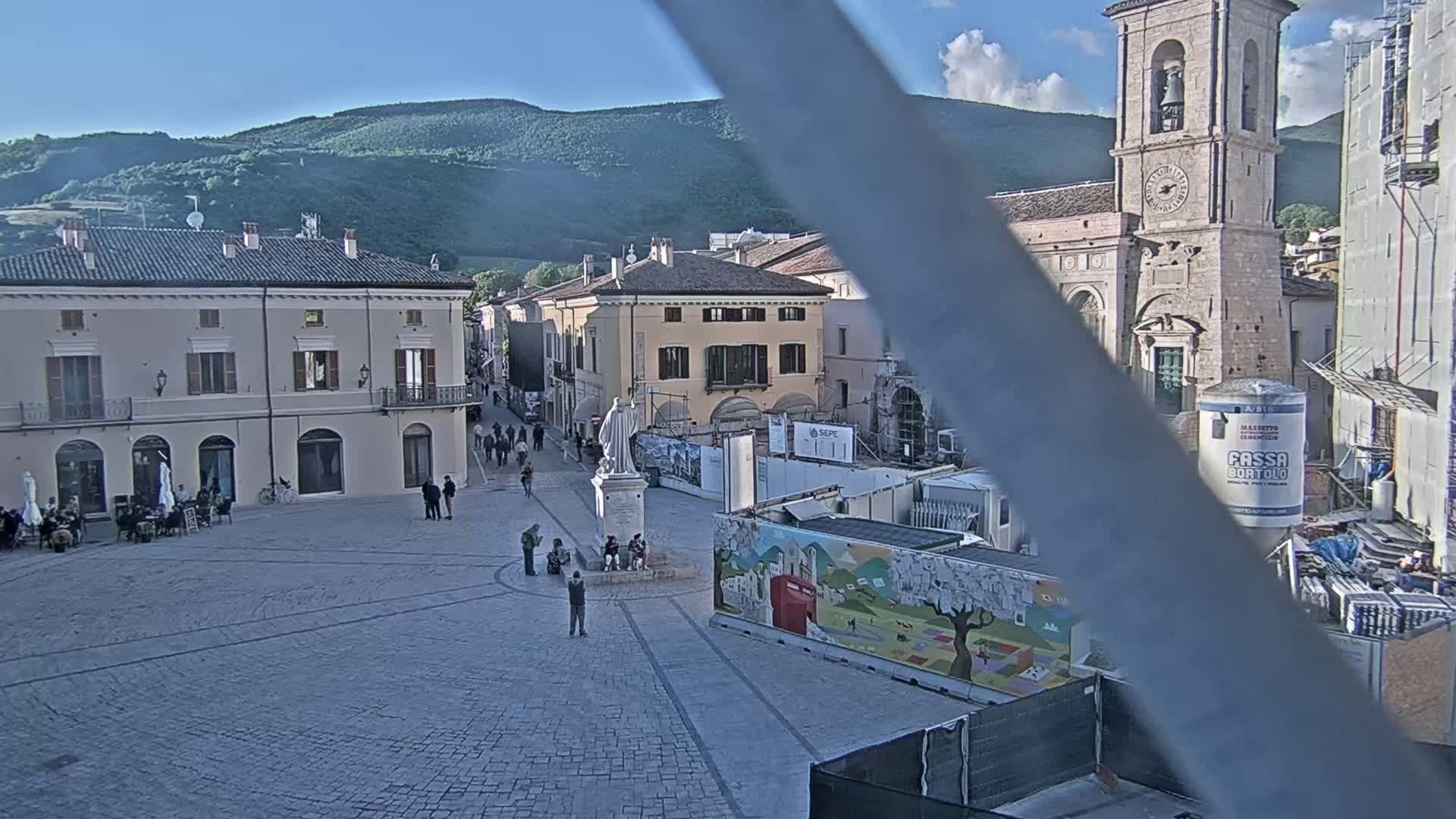 A mostly empty town square under a mostly clear sky, with buildings, a statue, and construction work visible.