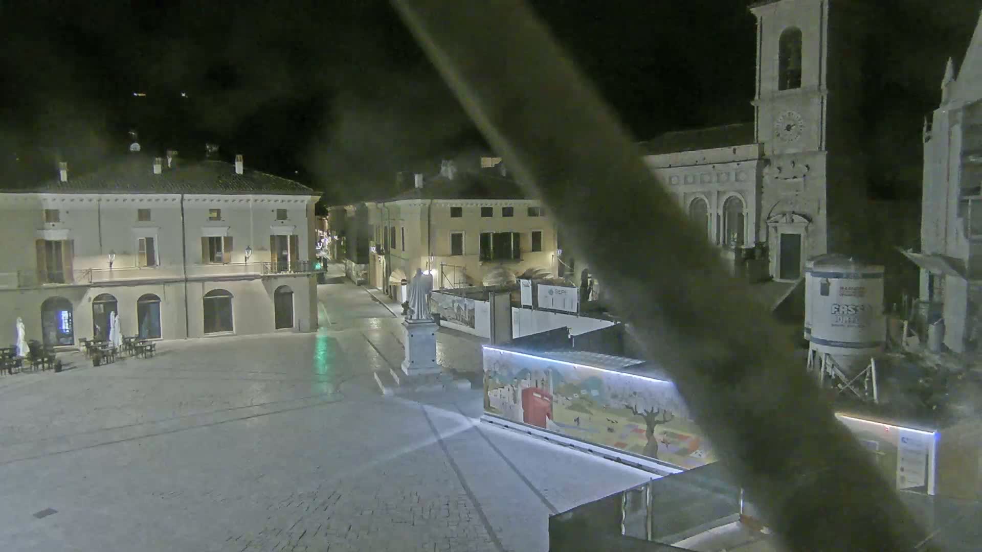 A nighttime view of a town square with several buildings, a statue, and construction equipment under clear skies.