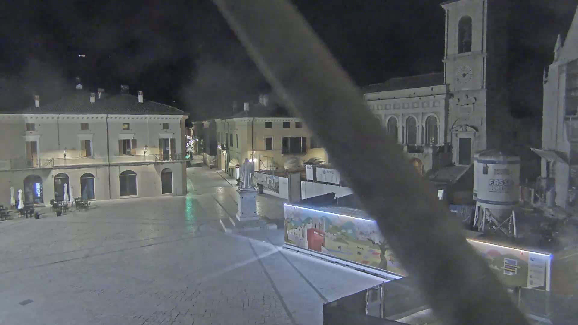 A nighttime view of a town square with several buildings, a statue, and construction equipment.