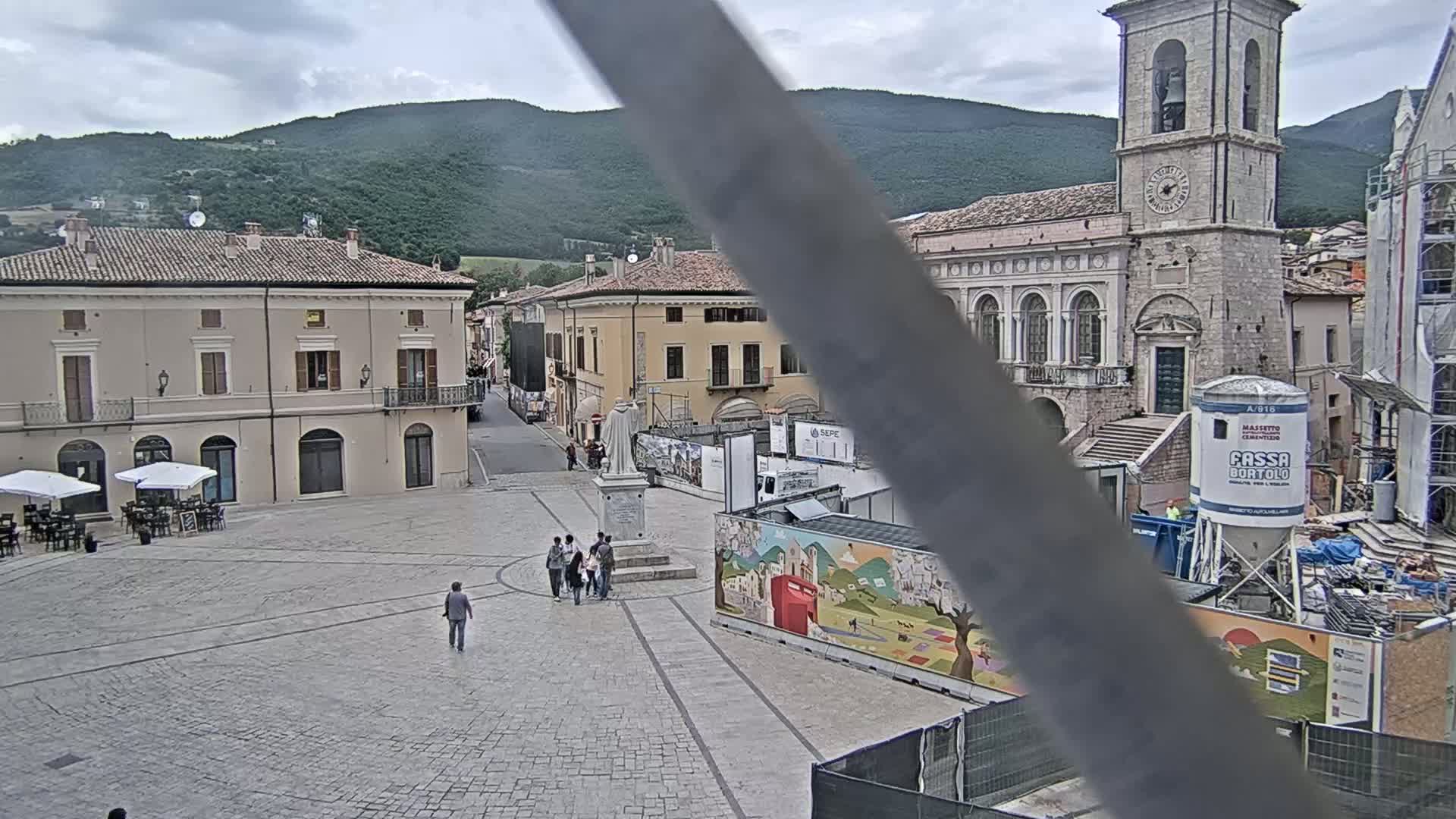 A town square with several buildings, a church with a tall bell tower, and some construction underway, all under an overcast sky.