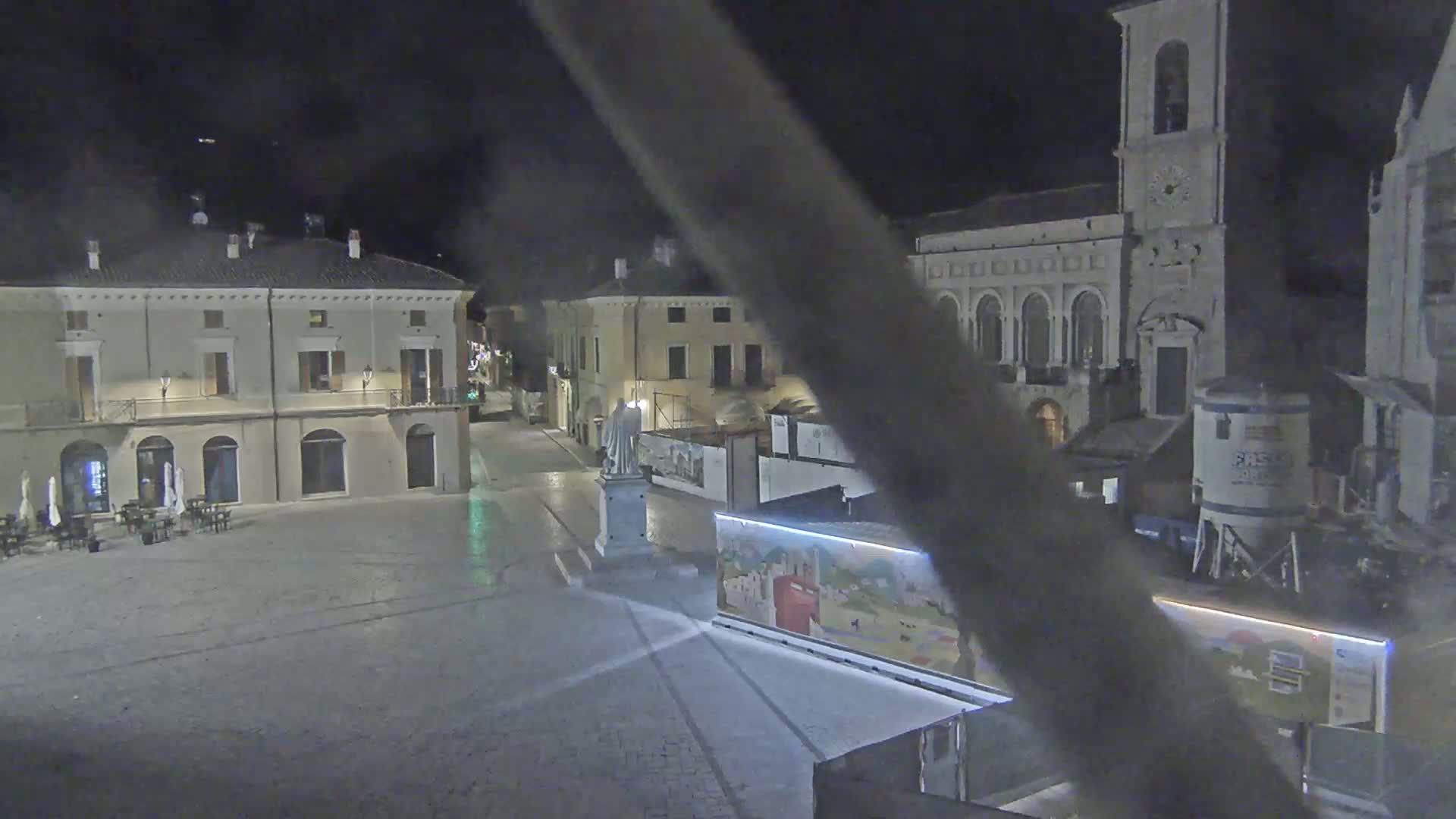 A nighttime view of a town square with several buildings, a statue, and construction equipment, under clear skies.
