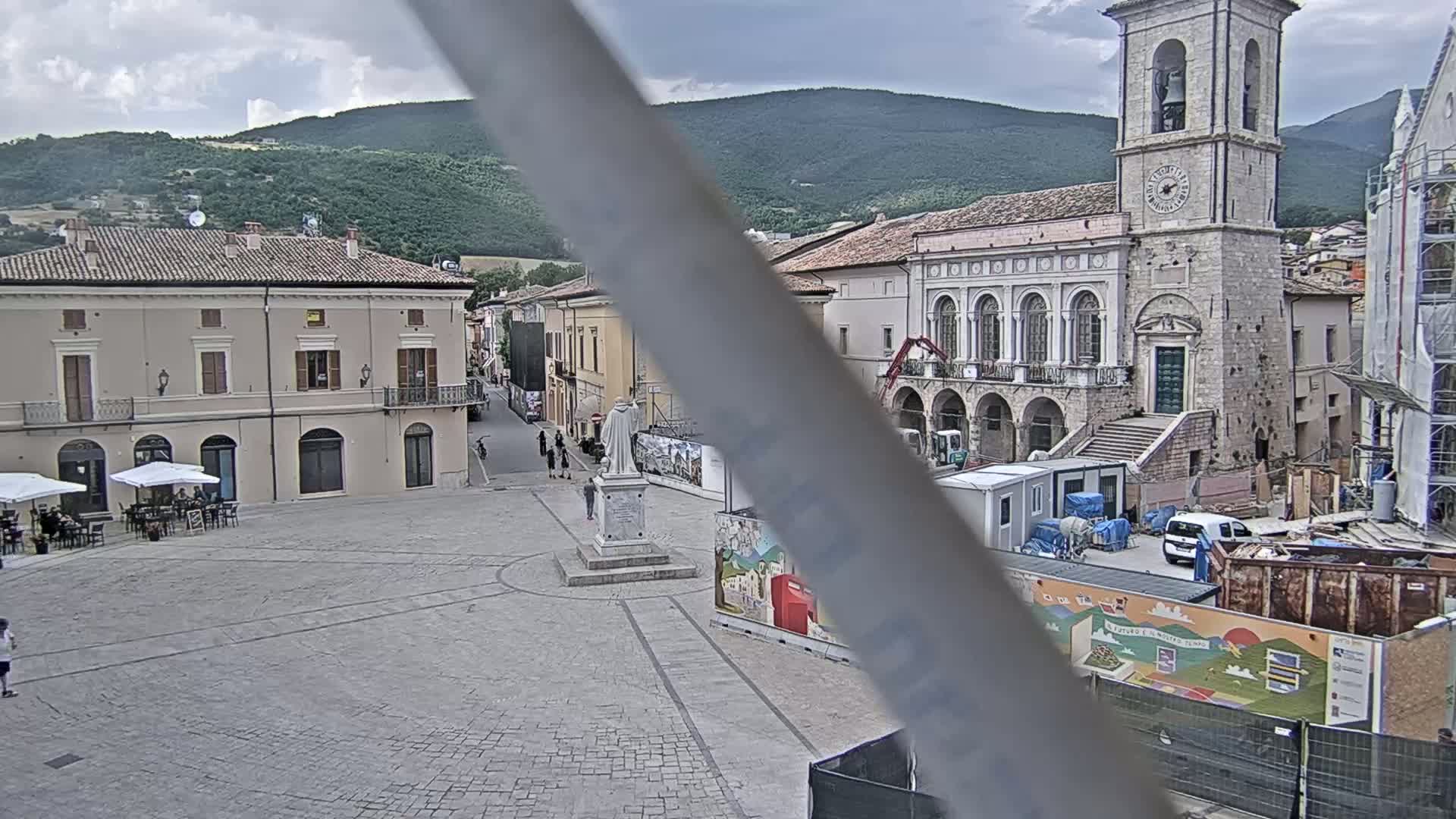 A town square with a statue, buildings, and a partially obscured view of mountains under a cloudy sky.