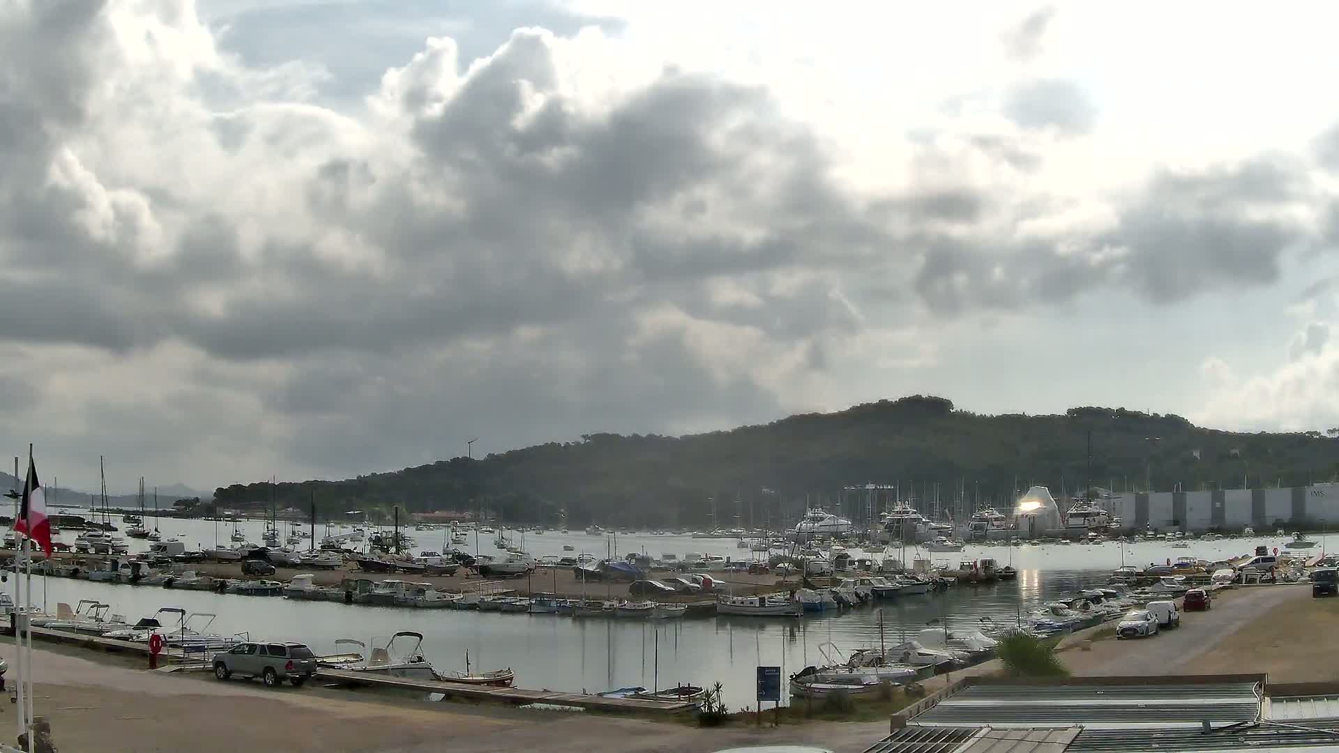 A harbor filled with numerous boats is nestled beside a hill under a cloudy sky.